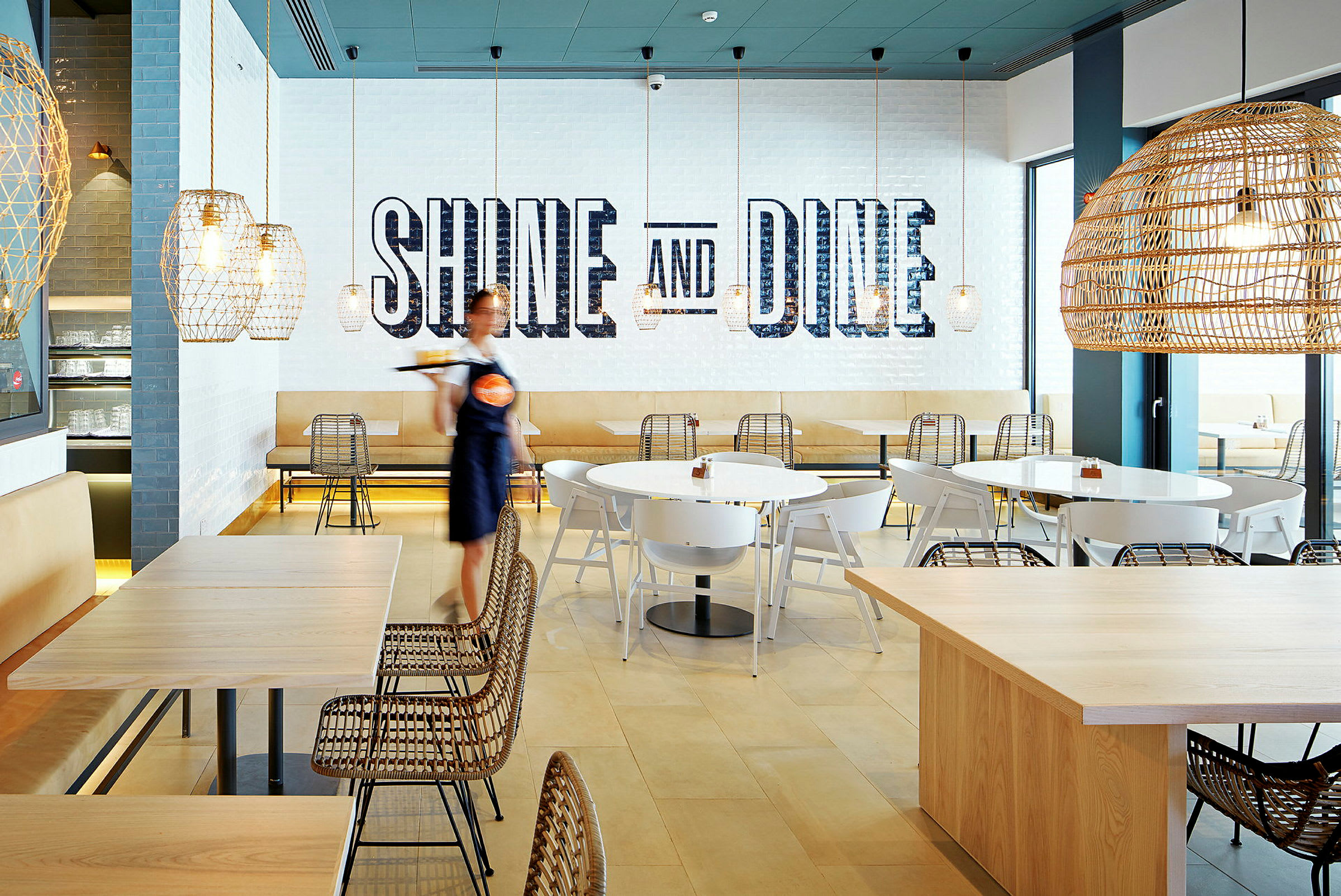 En moderne restaurant med siddepladser, belysning og tekst på væggen, der siger 'Shine and Dine'. (AI-genereret tekst)