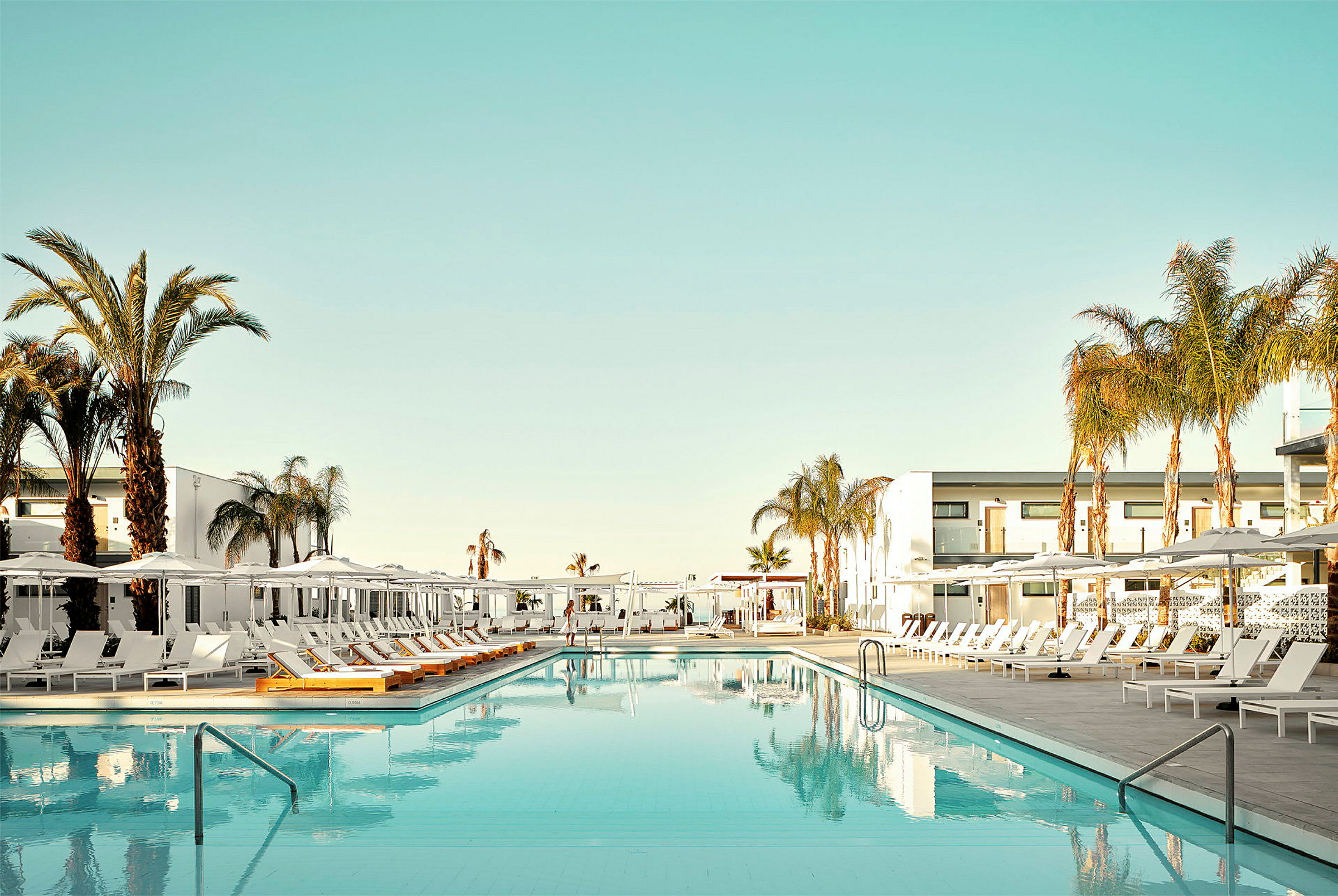 En swimmingpool omgivet af solsenge og palmer ved et hotel. (AI-genereret tekst)
