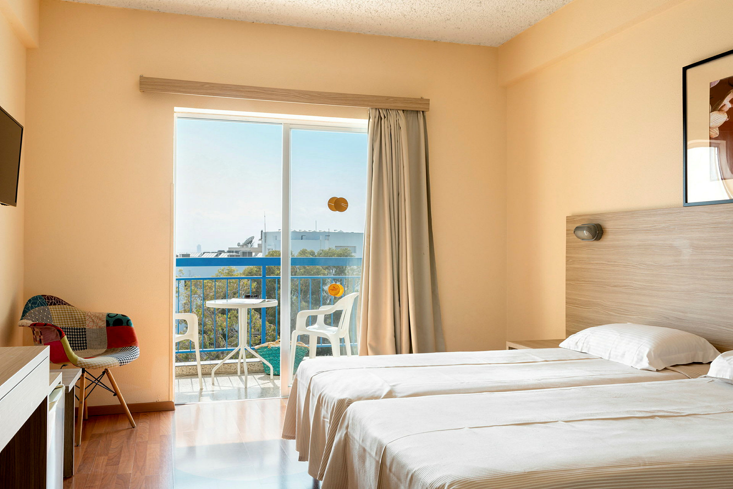 Et hotelværelse med to enkeltsenge, en stol, fjernsyn og en balkon med udsigt. (AI-genereret tekst)