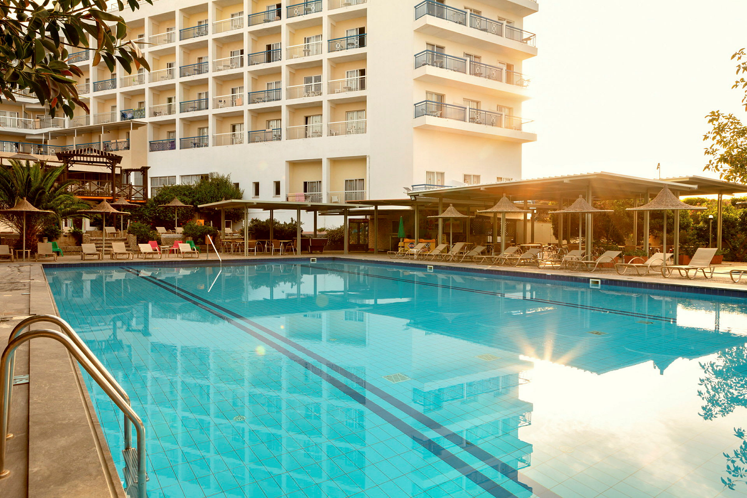 Udendørs swimmingpool ved et hotel med liggestole og parasoller omkring. (AI-genereret tekst)