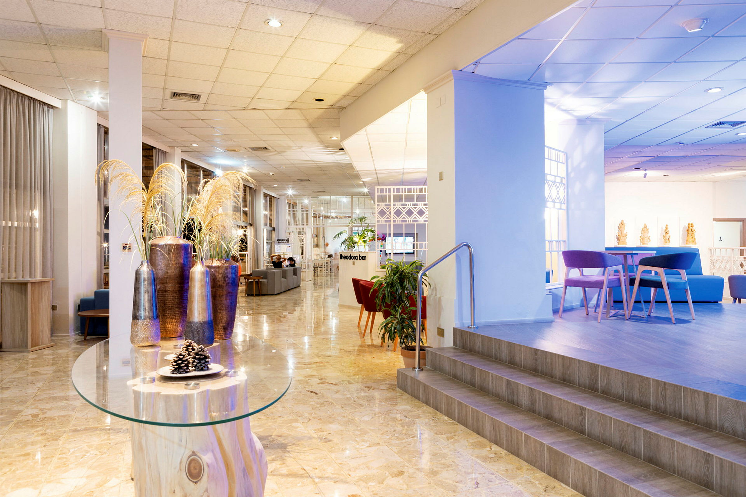 Billede af en hotellobby med moderne møbler og dekorationer. Et bord med dekorative genstande og et forhøjet siddeområde ses. (AI-genereret tekst)