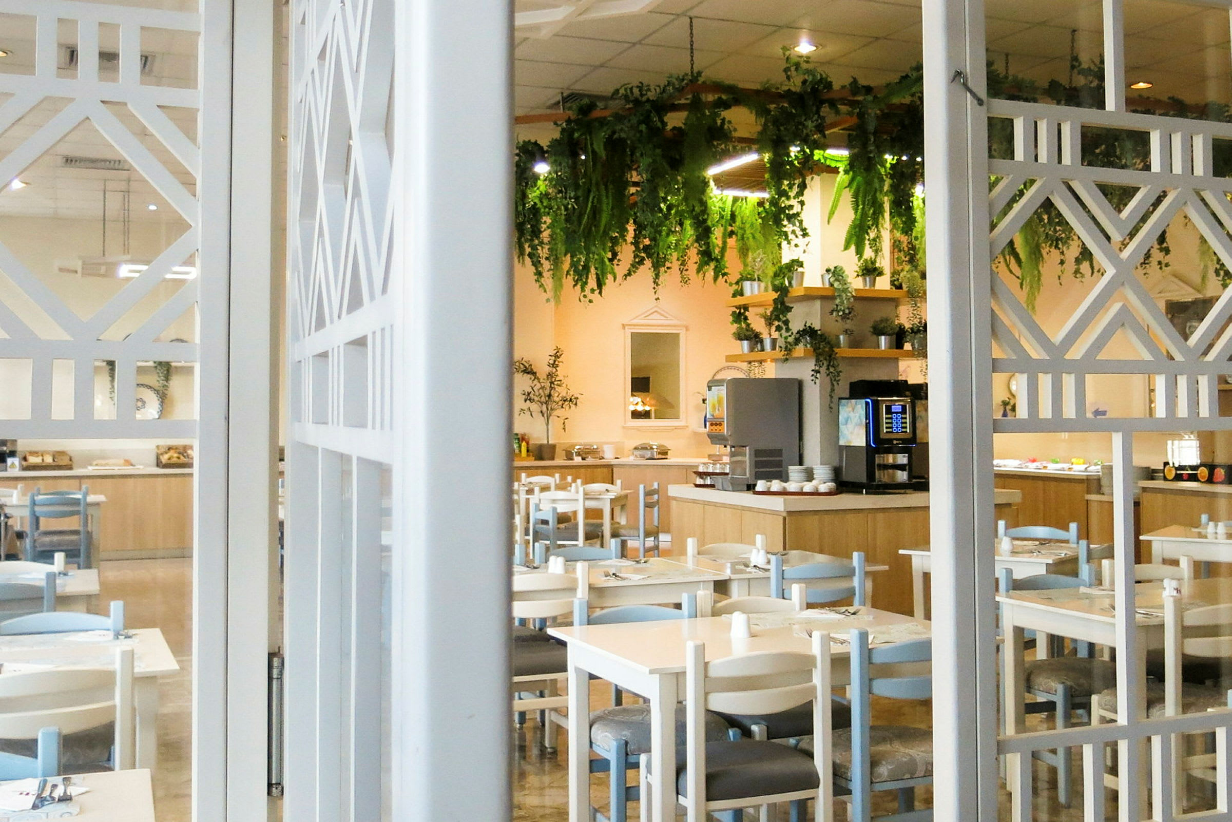 En restaurant med borde og stole, samt en dekoreret buffet og hængende vegetation. (AI-genereret tekst)