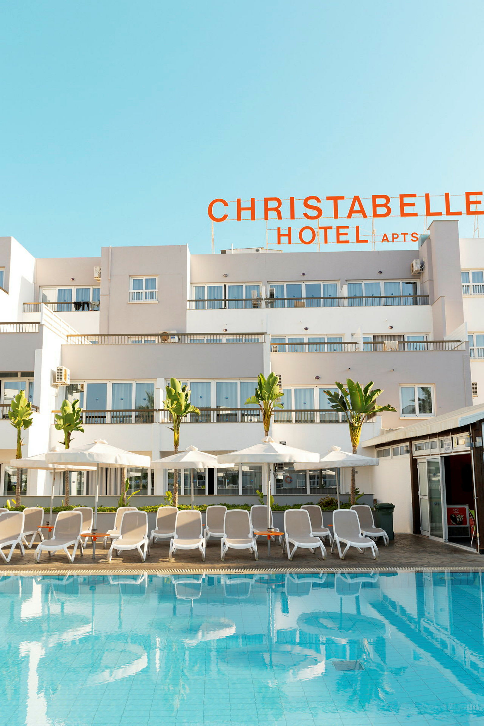 Udendørs pool med liggestole og parasoller foran Christabelle Hotel. (AI-genereret tekst)