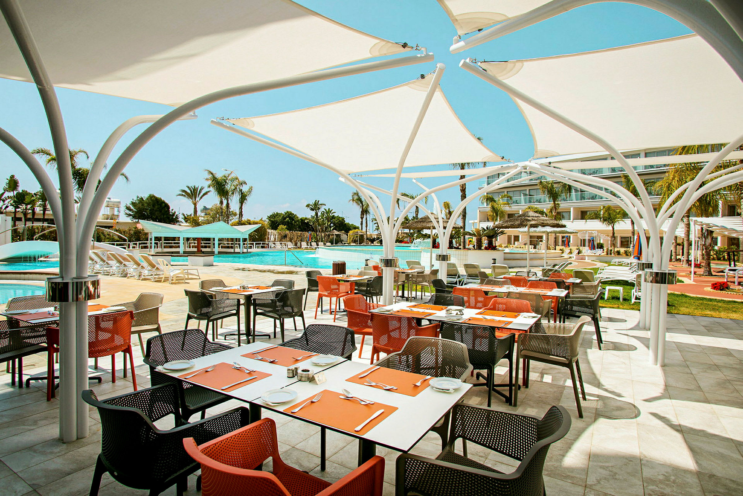 Udendørs restaurant med farverige stole og borde tæt på en pool. (AI-genereret tekst)