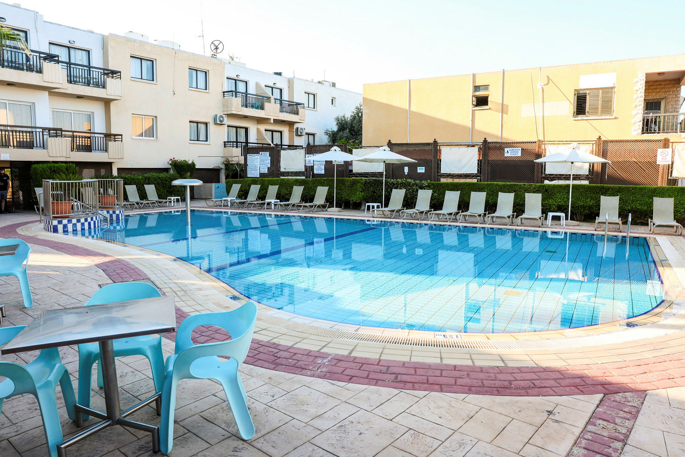 En pool med omkringliggende liggestole og parasoller ved et hotelkompleks. (AI-genereret tekst)