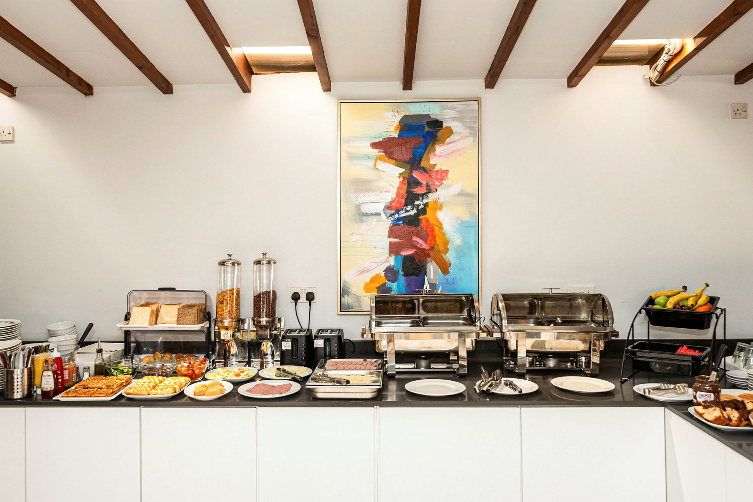 Buffet med forskellige morgenmadsvalg og et farverigt maleri ovanover. (AI-genereret tekst)