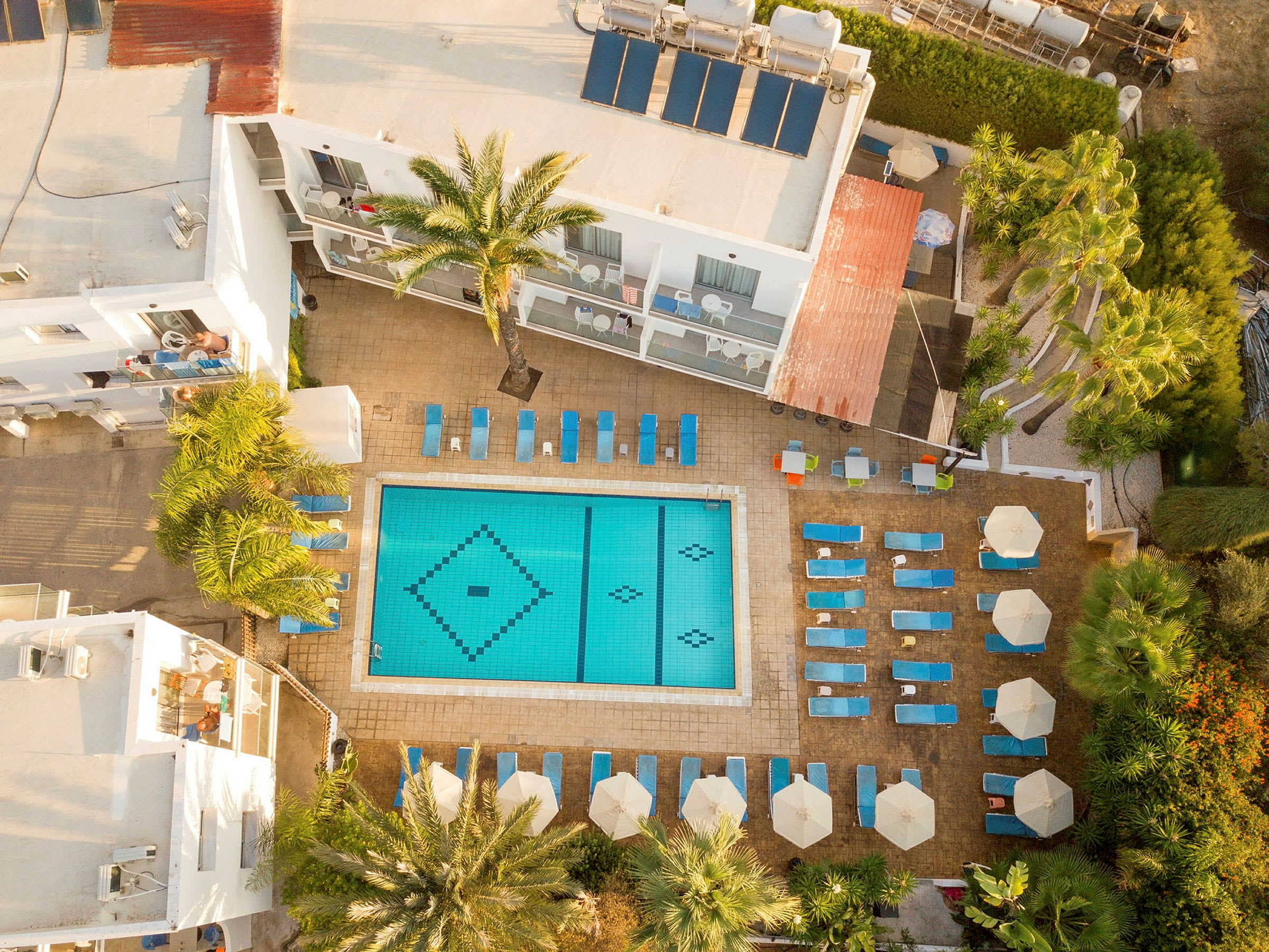 Luftfoto af hotelpool med liggestole og parasoller omkring. (AI-genereret tekst)