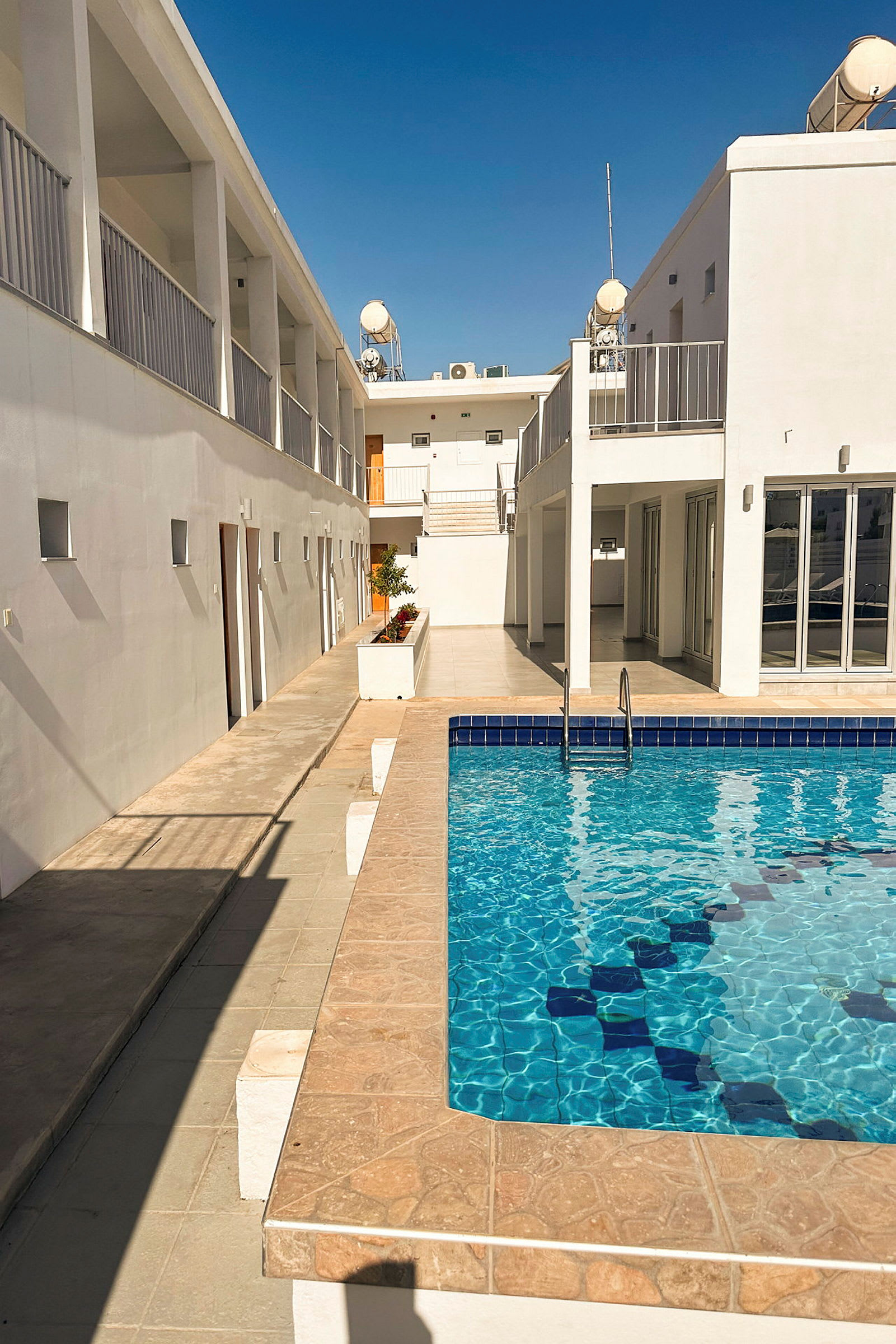 Billede af et hotelområde med hvid bygning og swimmingpool. (AI-genereret tekst)