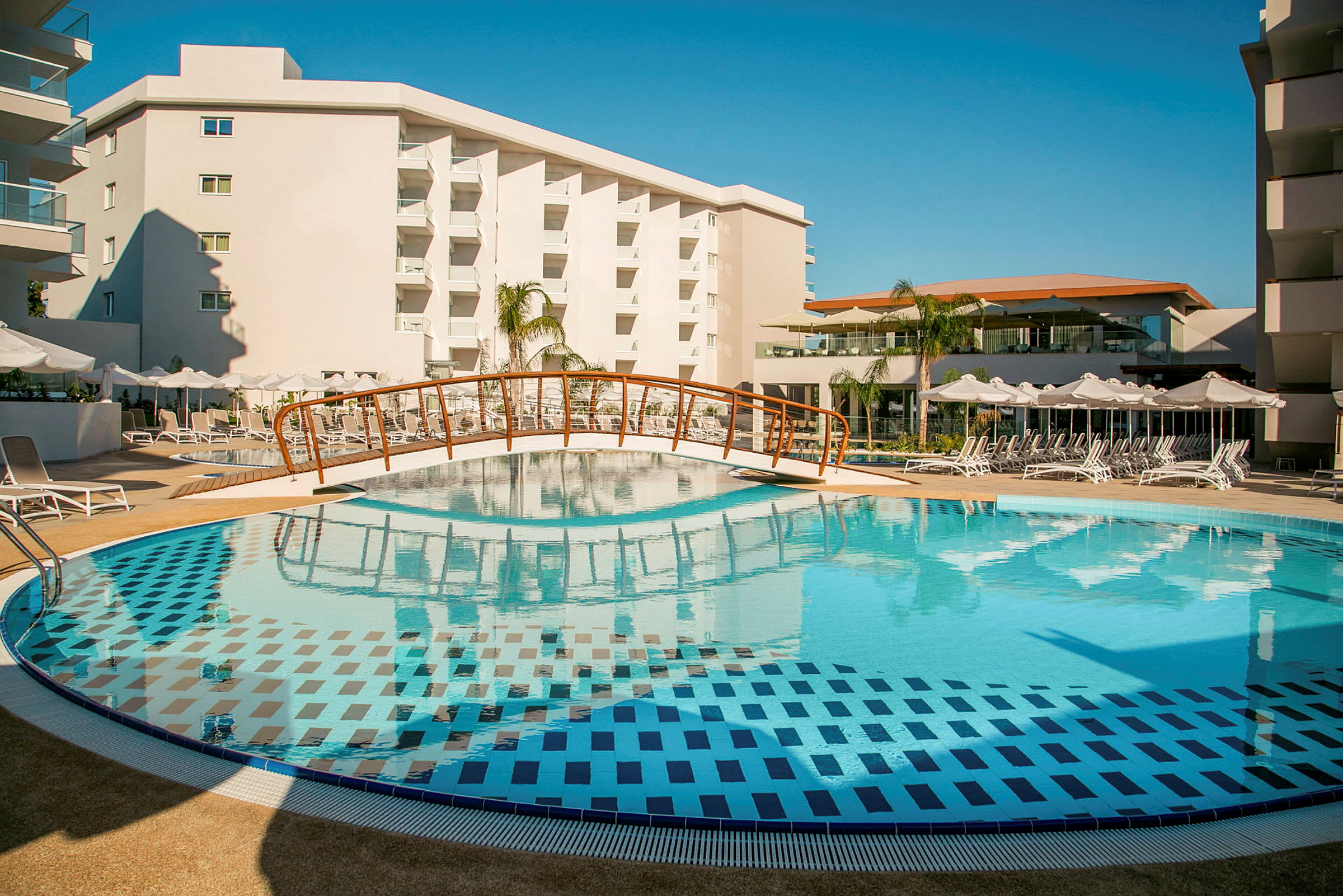 En swimmingpool ved et feriehotel med liggestole og en lille bro over vandet. (AI-genereret tekst)