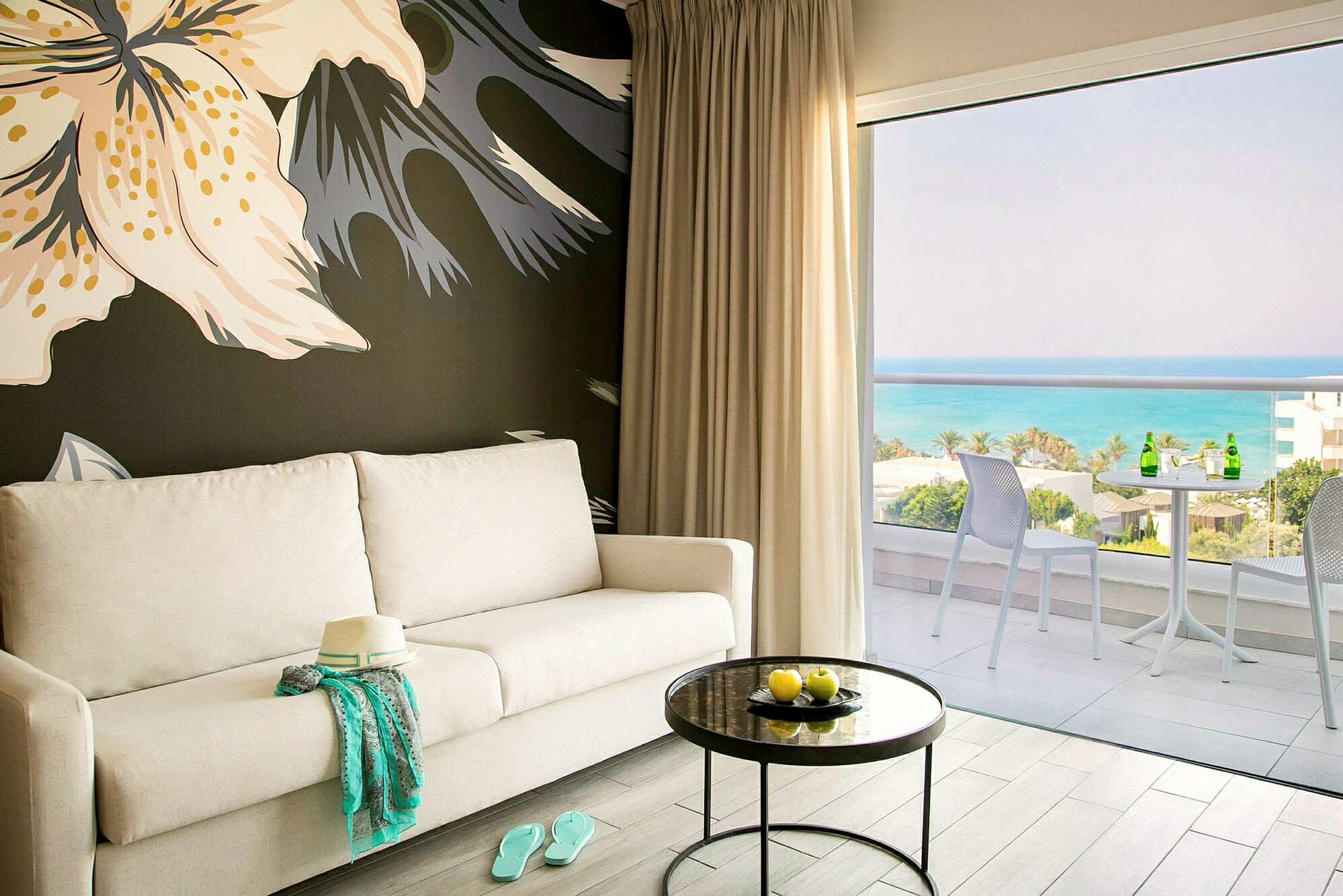 Et rum med lys sofa, rundt bord med gule frugter og balkon med udsigt over havet. (AI-genereret tekst)