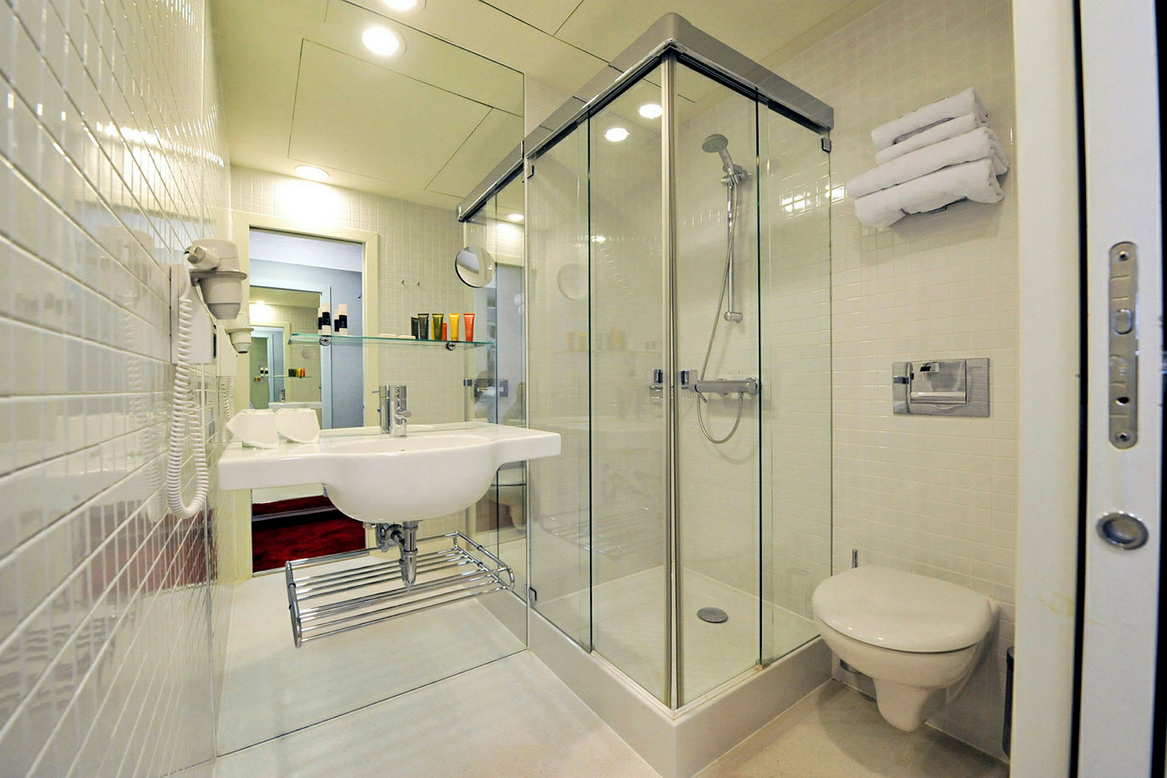 Hotelbadeværelse med brusekabine, håndvask og toilet. (AI-genereret tekst)