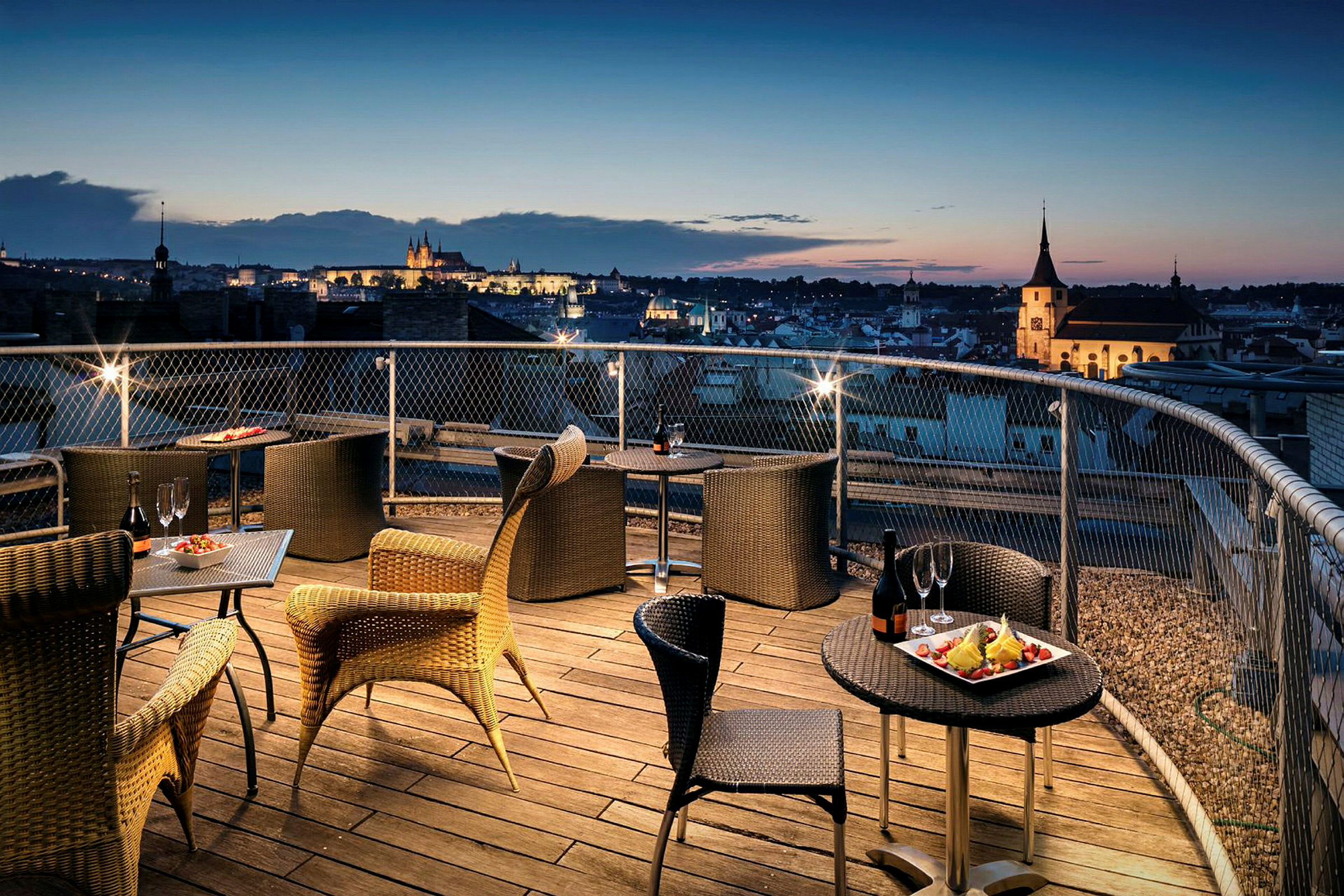 Terrasse med siddepladser og udsigt over by ved solnedgang. (AI-genereret tekst)