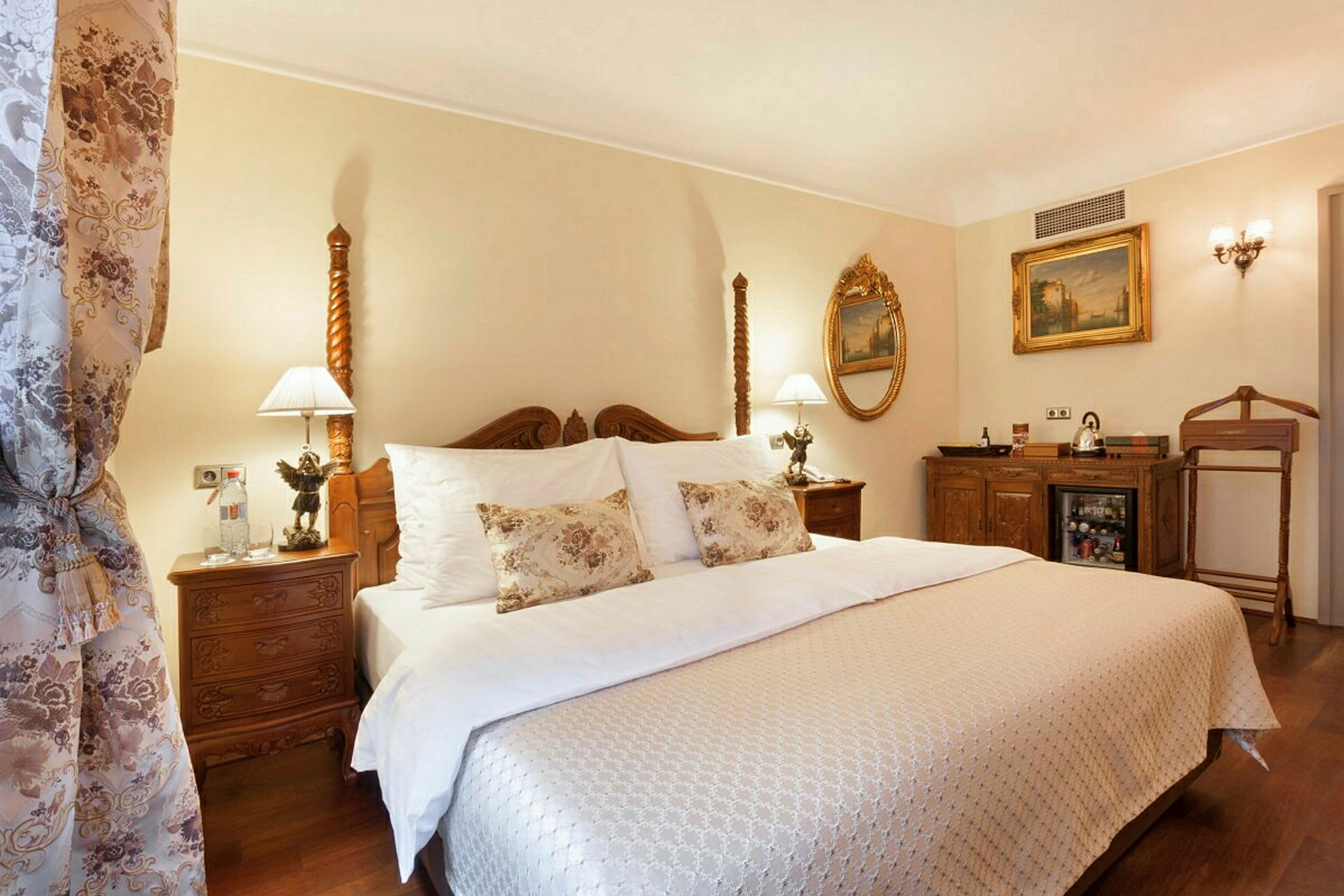 Et elegant hotelværelse med en dobbeltseng klædt i hvide og mønstrede tekstiler, dekorationer i klassisk stil og lamper på sengebordene. (AI-genereret tekst)