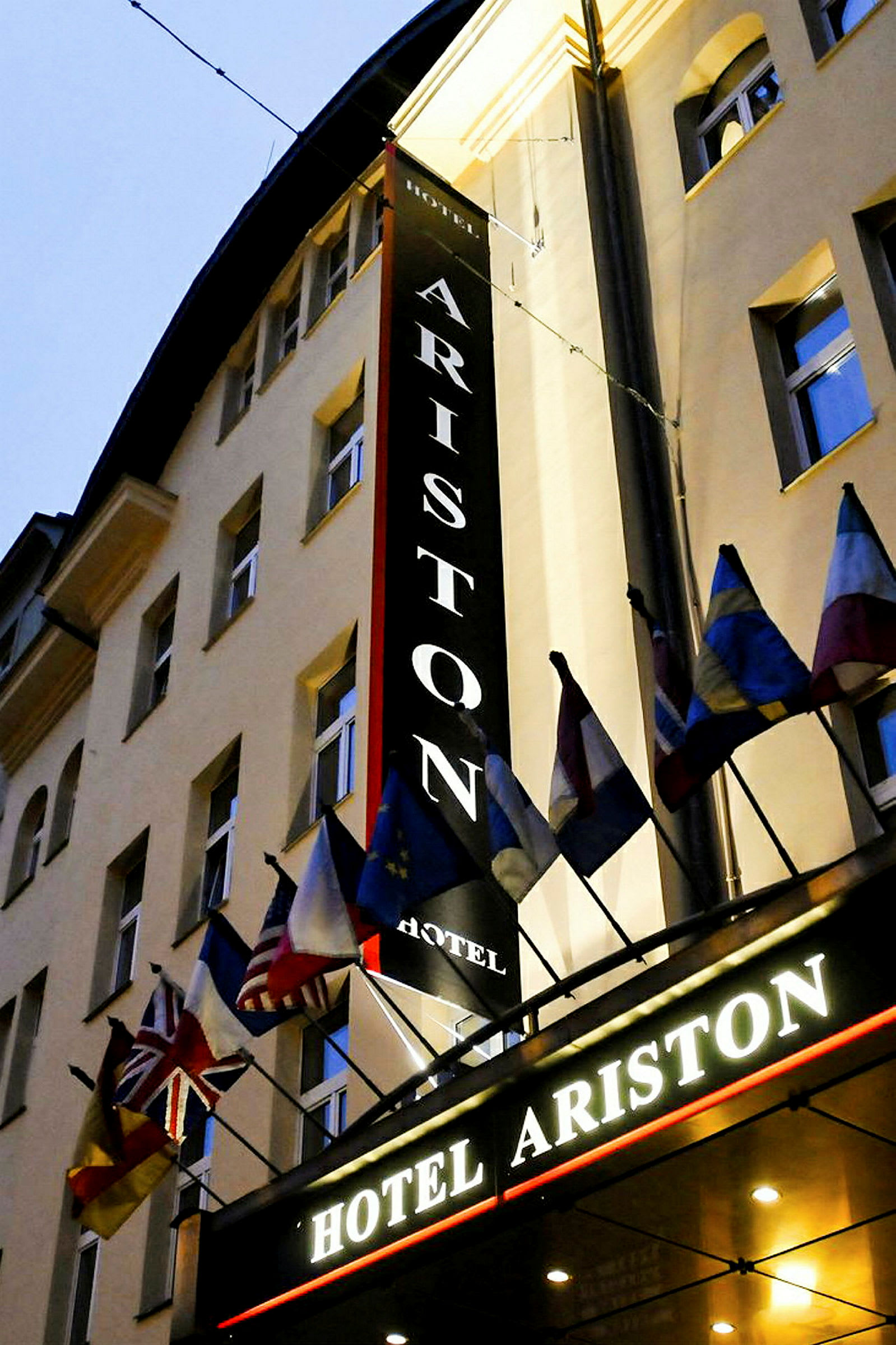 En hotelbygning med skilte, der står 'Hotel Ariston' og flere nationalflag over indgangen. (AI-genereret tekst)