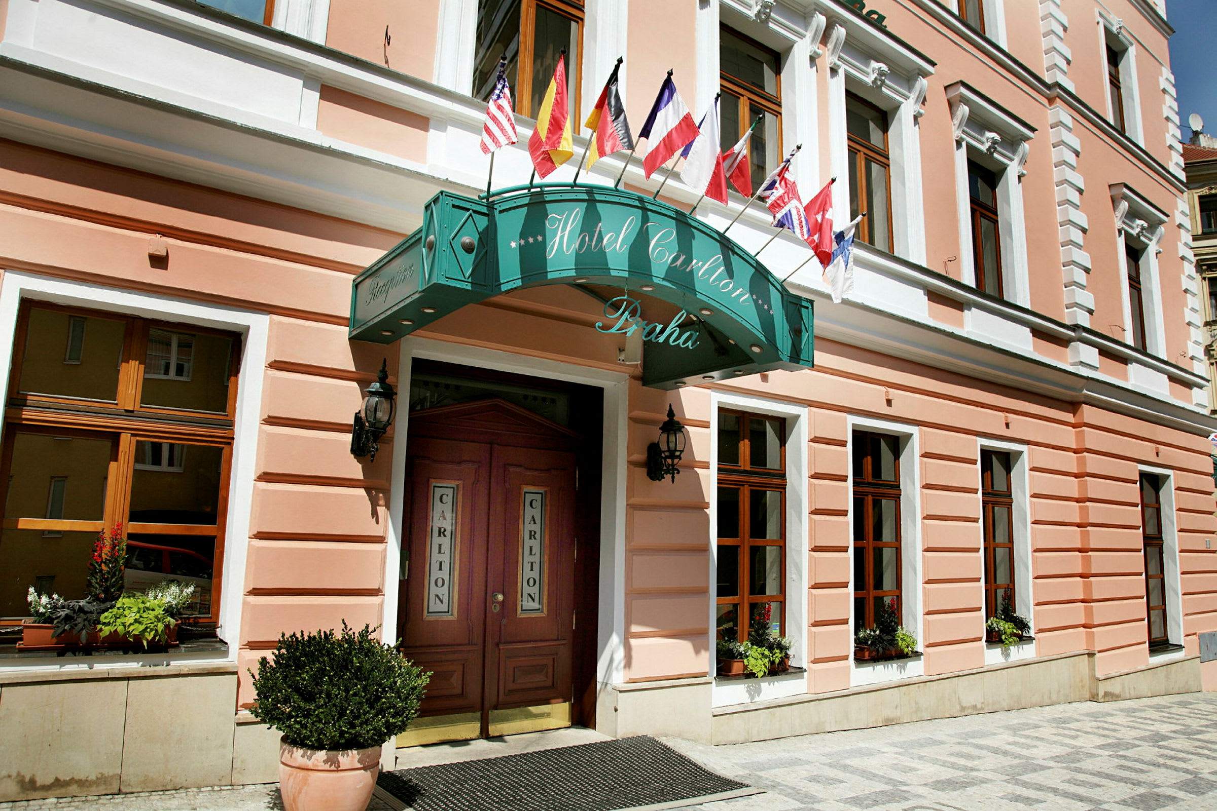 Billede af facaden på et hotel med skilt og dekorationer, med flere nationalflag over indgangen. (AI-genereret tekst)