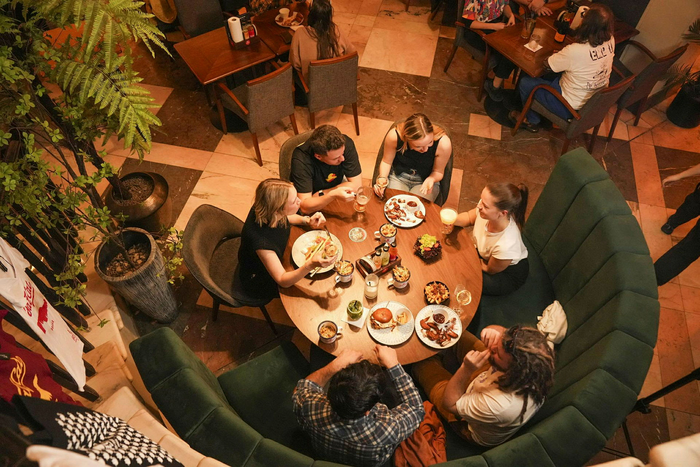 Fem personer sidder rundt om et rundt bord på en restaurant og spiser og drikker. (AI-genereret tekst)