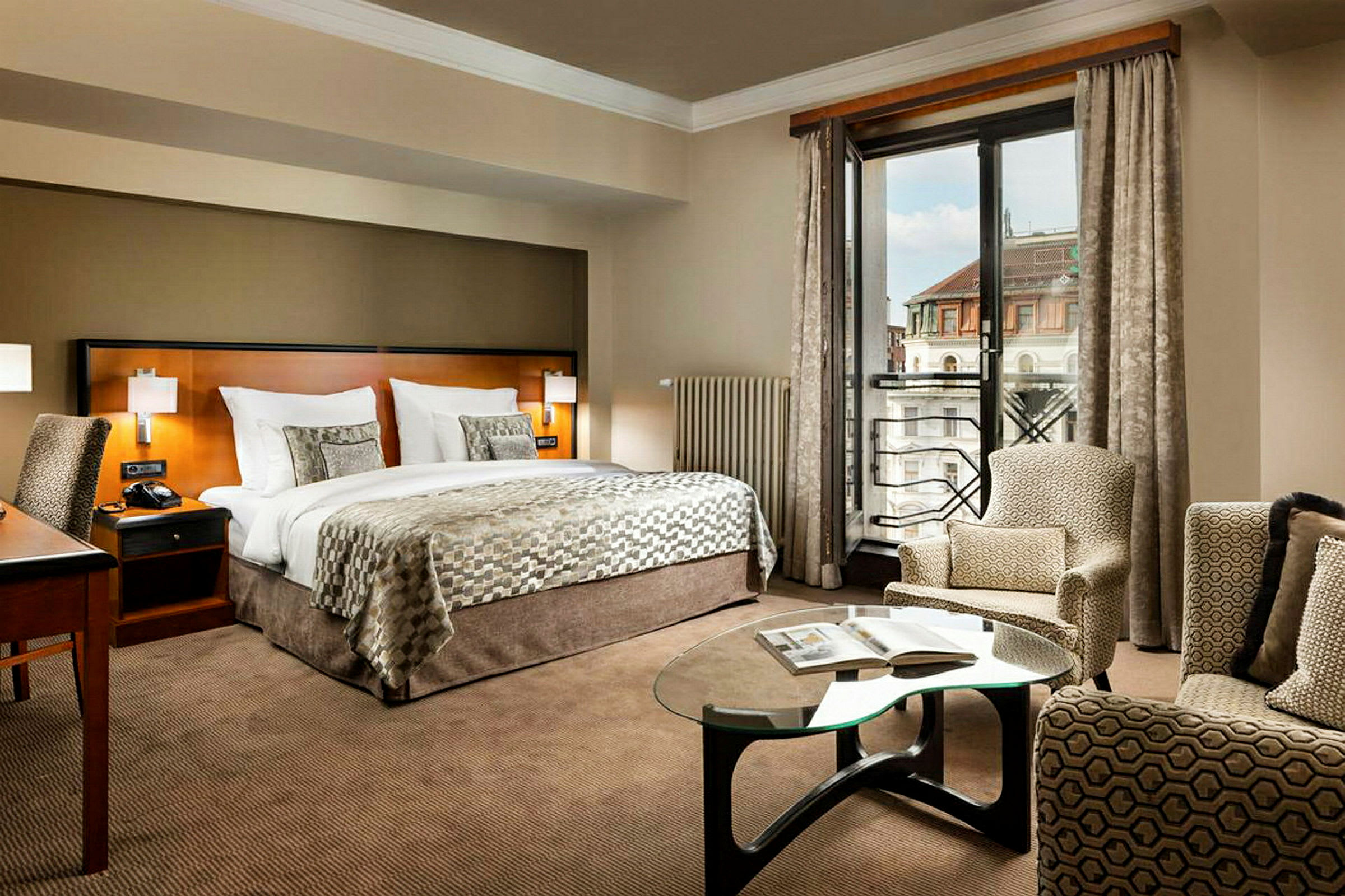 Et elegant hotelværelse med en dobbeltseng, et arbejdsområde, en siddesektion og et vindue med udsigt over byen. (AI-genereret tekst)