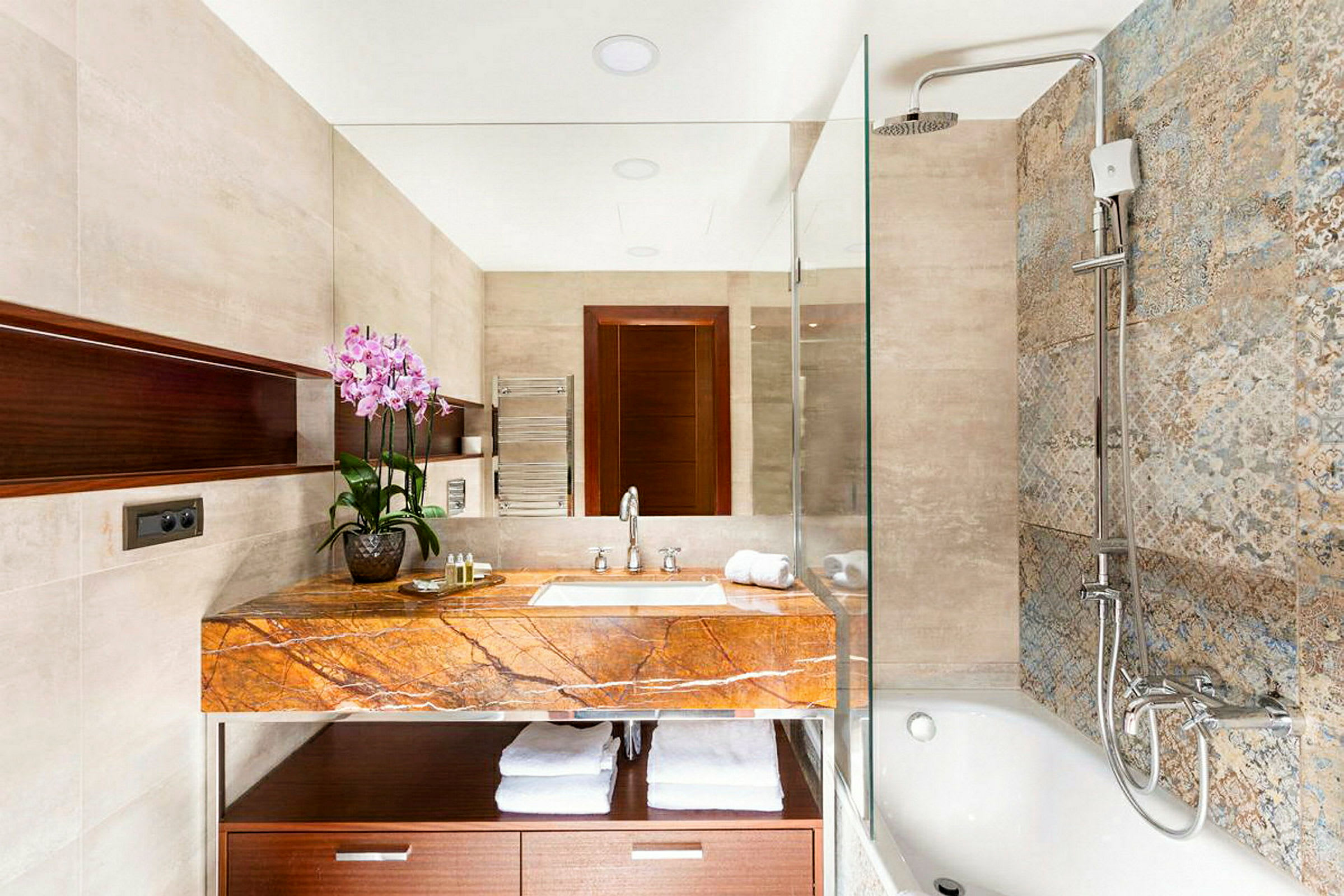 Et moderne badeværelse med en håndvask og en stenbordplade, et spejl samt en bruser og et badekar. (AI-genereret tekst)