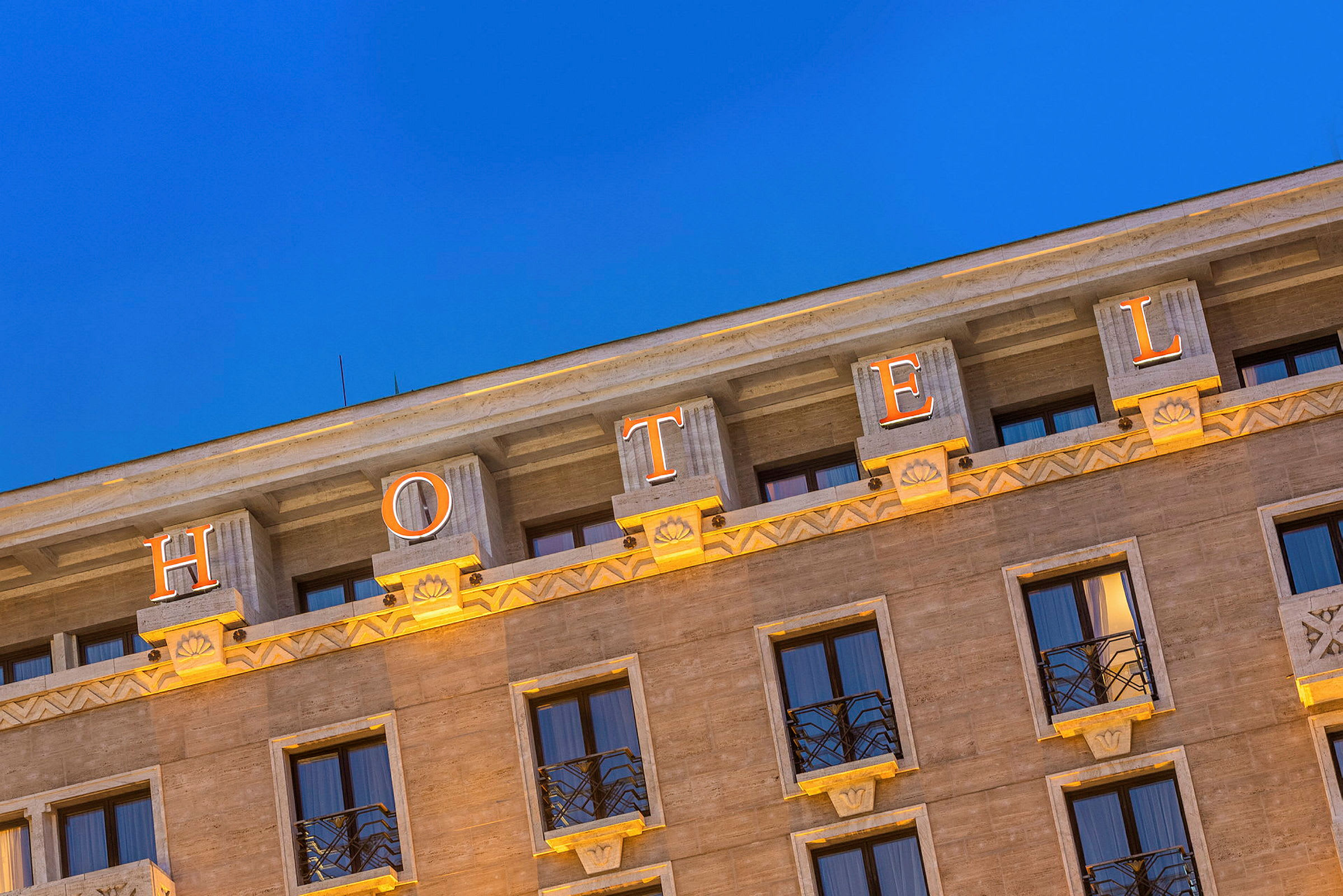 Facaden af et hotel med oplyste bogstaver, der staver ordet 'HOTEL', mod en klarblå aftenhimmel. (AI-genereret tekst)