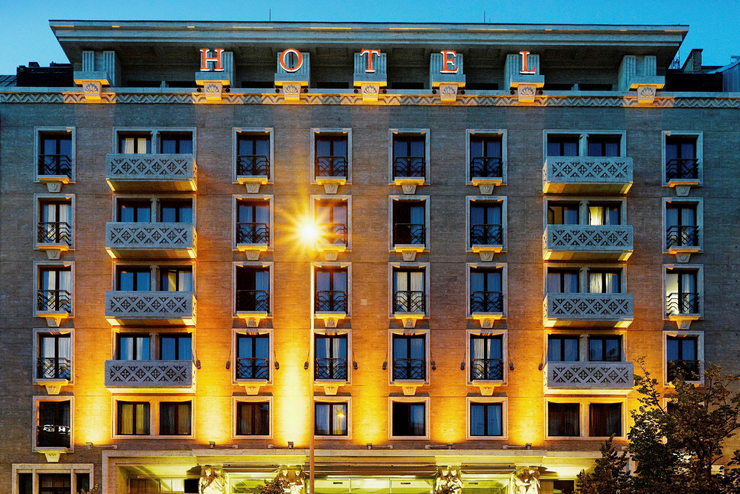 En flerfarvet hotelbygning med altaner og stor oplyst skiltindskrift "HOTEL" på toppen. (AI-genereret tekst)