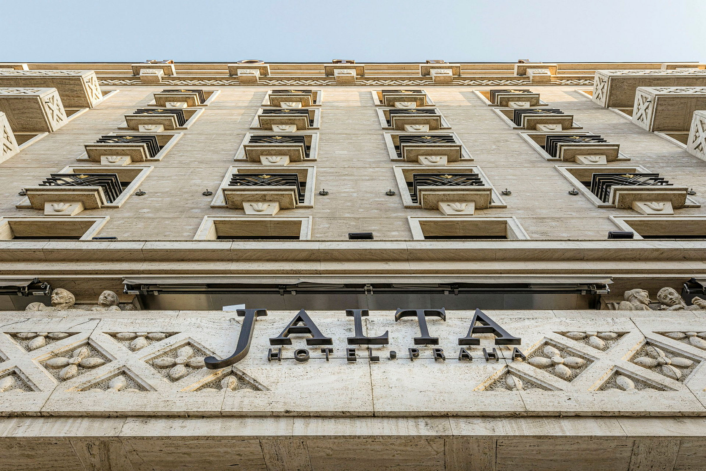 En bygningsfacade fotograferet nedefra og op, med et skilt, hvorpå der står "Jalta Hotel Praha". (AI-genereret tekst)