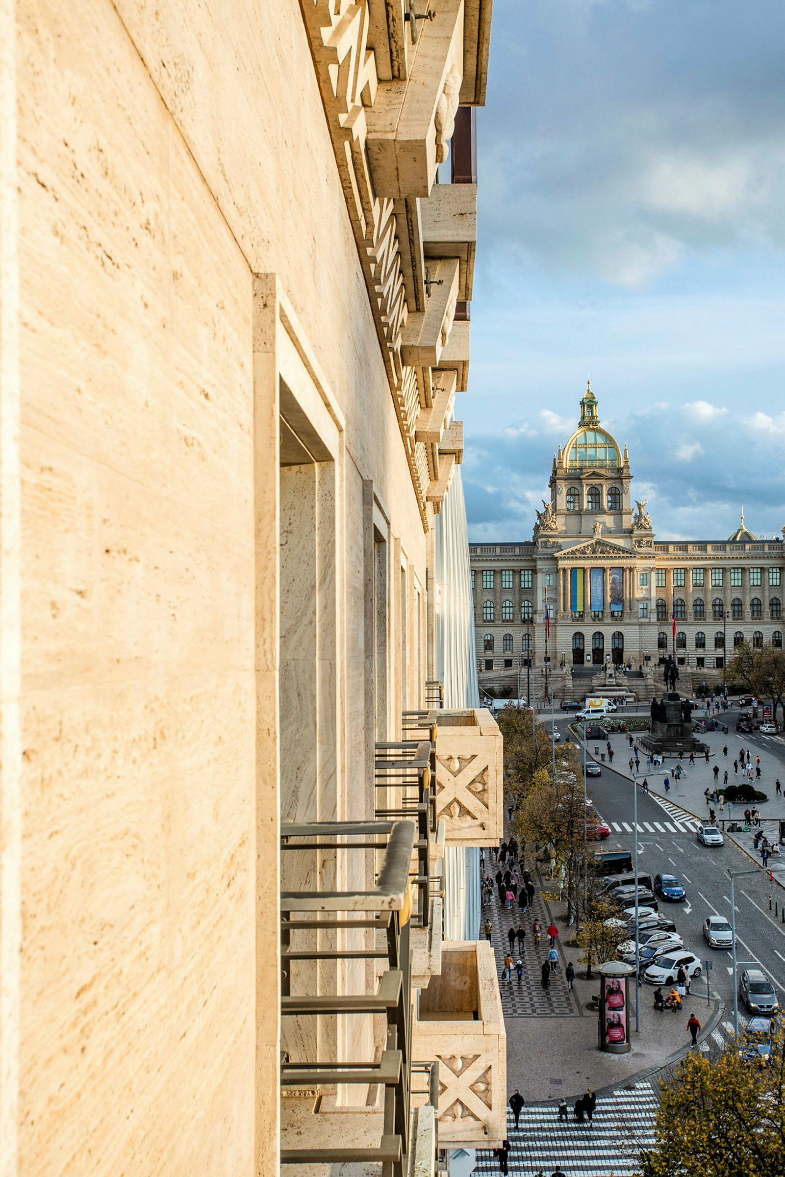 Billede af en bygningfacade i forgrunden og en bygning med en kuppel i baggrunden, samt en travl gade med mennesker og trafik i midten. (AI-genereret tekst)