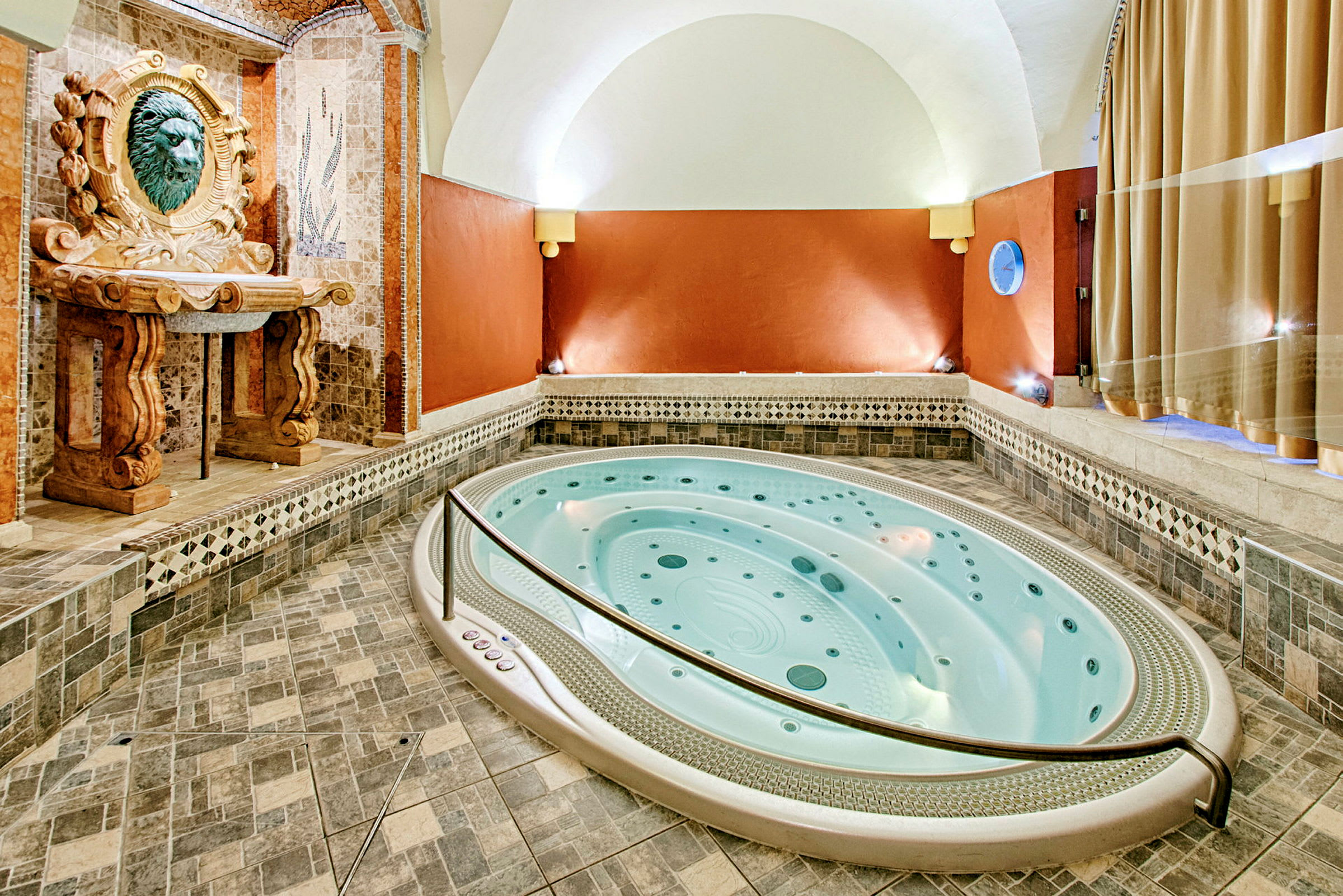 En indendørs jacuzzi med mosaik og dekorative ornamenter på væggene og gulvet. (AI-genereret tekst)