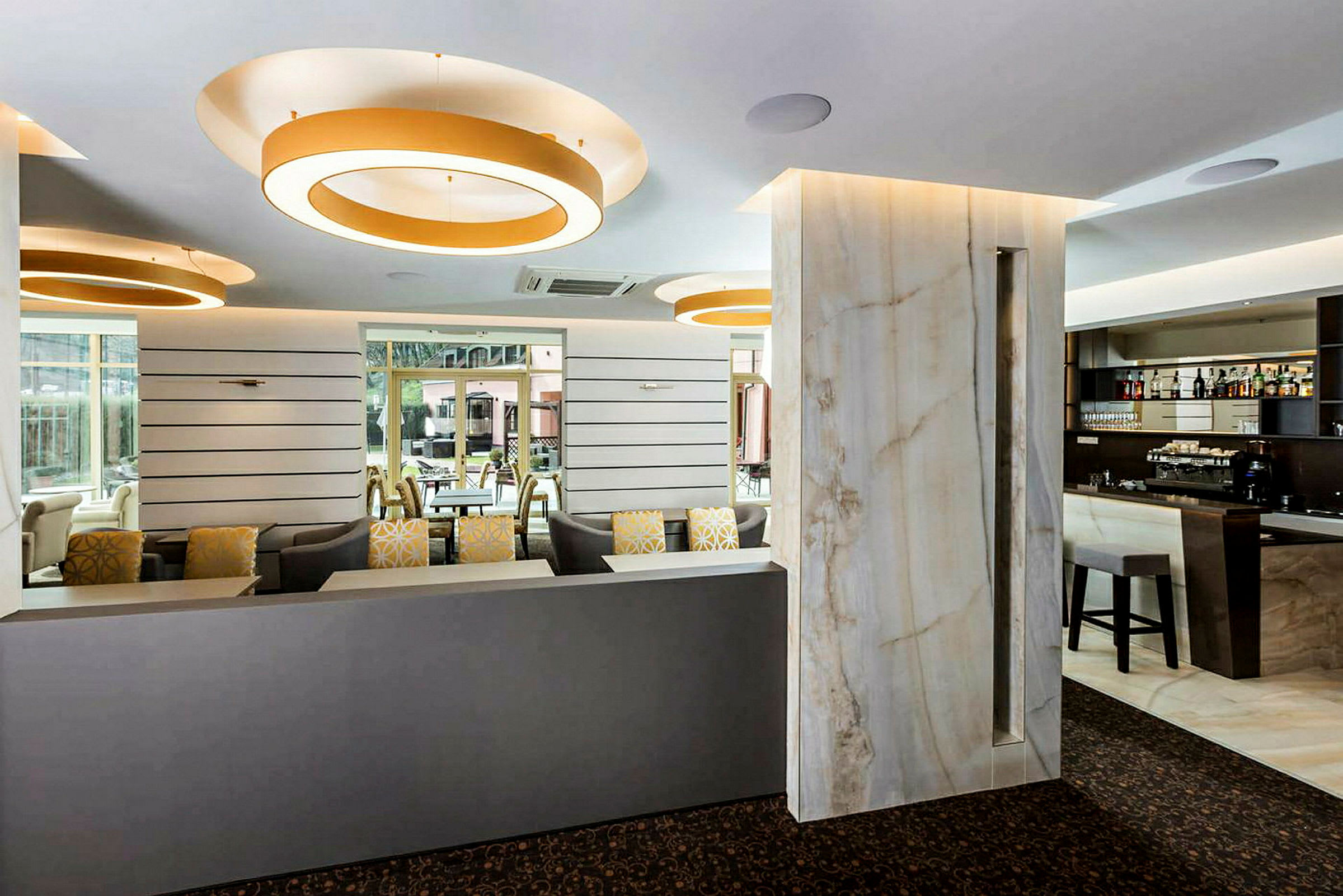 Interiør af en moderne lounge med sofaer, barområde og store dekorative lysringe i loftet. (AI-genereret tekst)