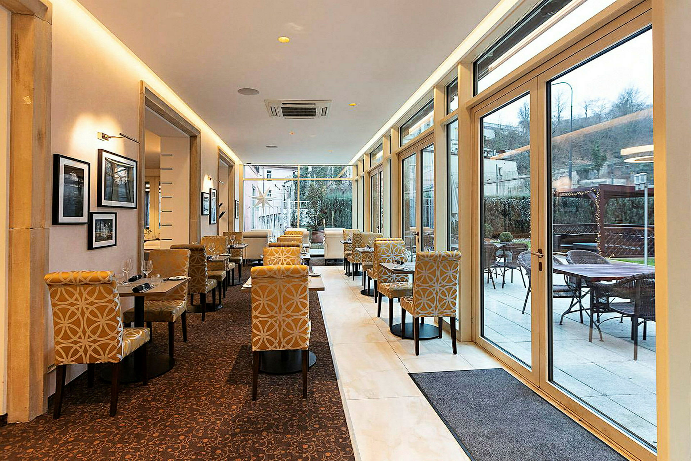 Billede af en restaurant eller café med elegante møbler og store vinduer, der lukker masser af lys ind. (AI-genereret tekst)