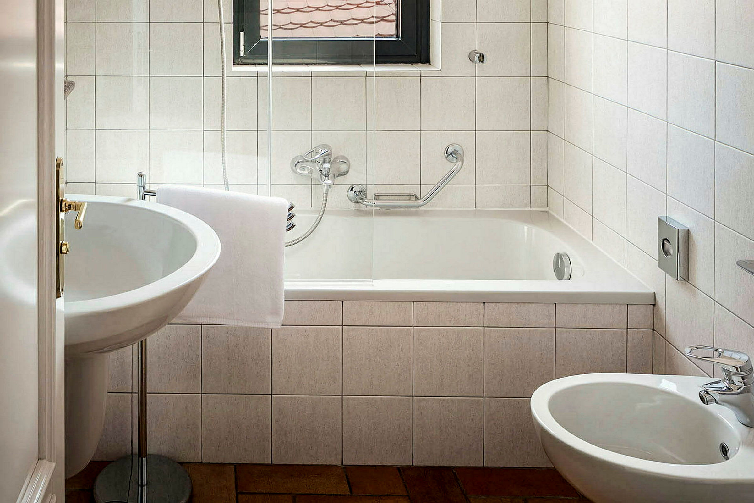 Et badeværelse med badekar, håndvask og bidet. Hvide fliser på væggene. (AI-genereret tekst)
