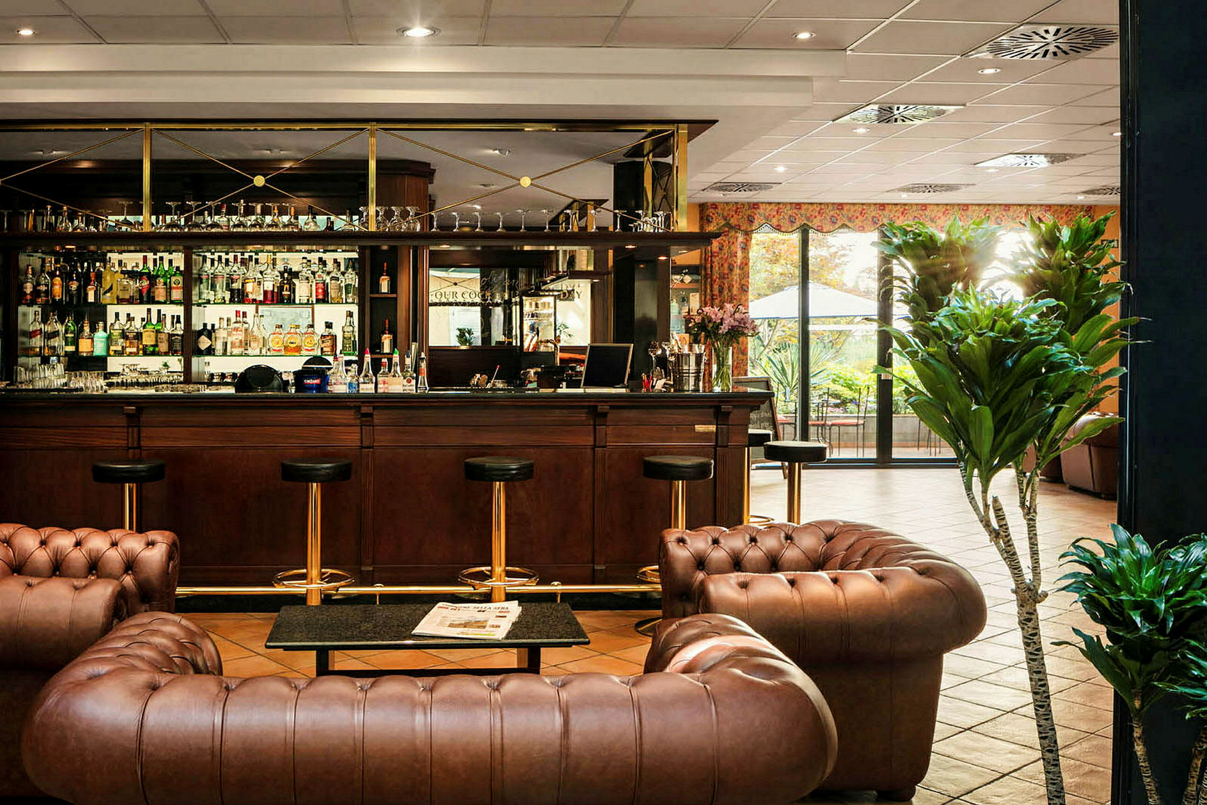 Billede af en hotelbar med klassisk indretning i brunt læder og træ. Foran er en sofagruppe, og i baggrunden ses en velassorteret bardisk. (AI-genereret tekst)