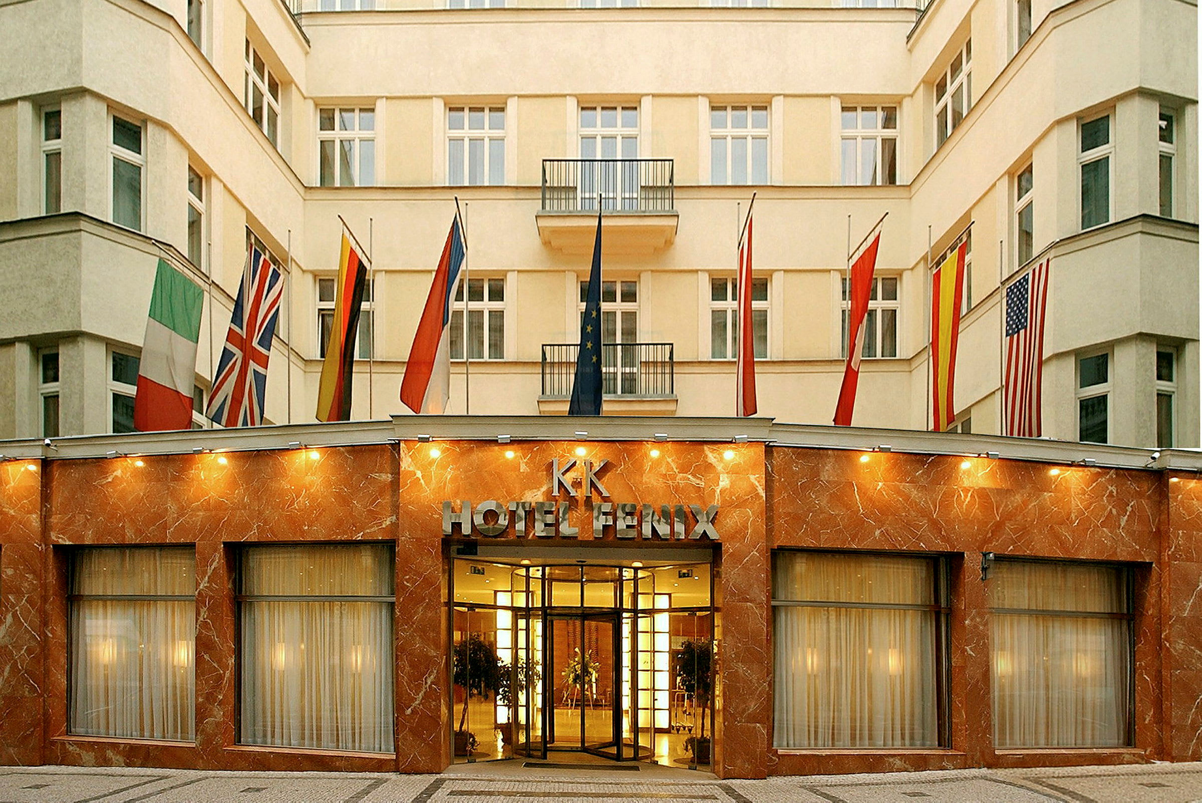 Bygningen er et hotel med facade af marmor og glas samt flere flag ved indgangen. (AI-genereret tekst)