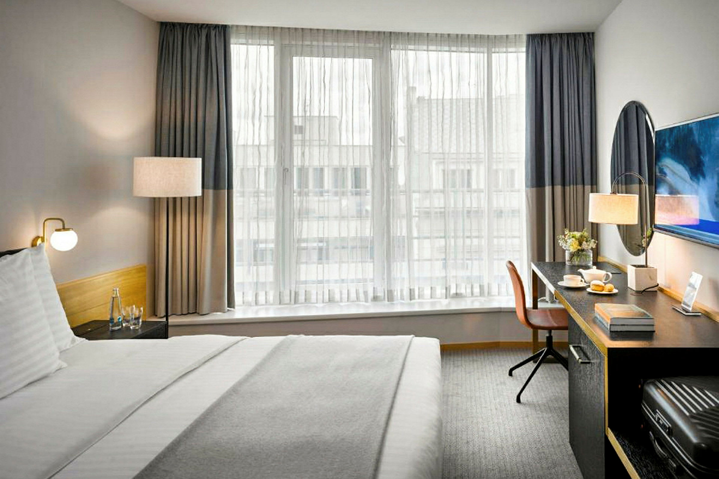Et hotelværelse med en seng, et skrivebord og et vindue med tynde gardiner. (AI-genereret tekst)