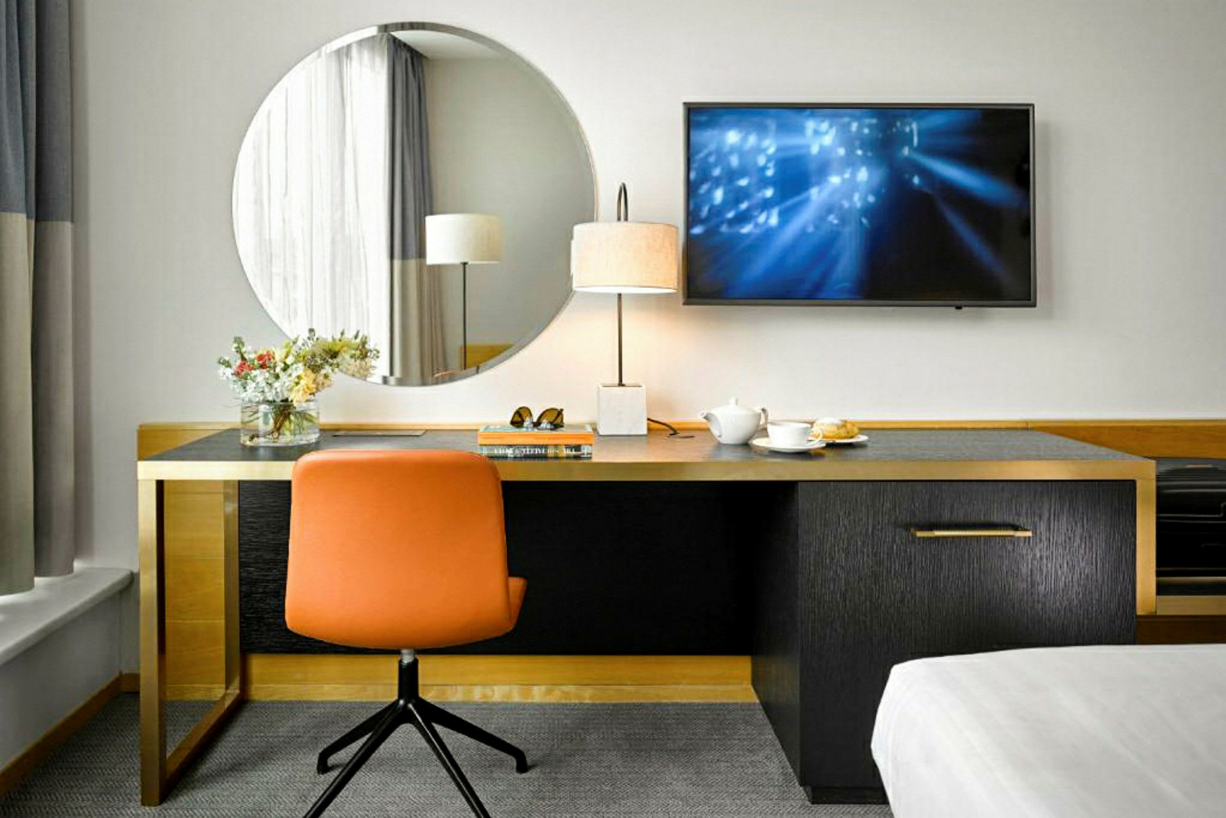 Et skrivebord med et rundt spejl ovenover, en orange stol og en bordlampe ved siden af. En kop te og nogle genstande ligger på skrivebordet. (AI-genereret tekst)