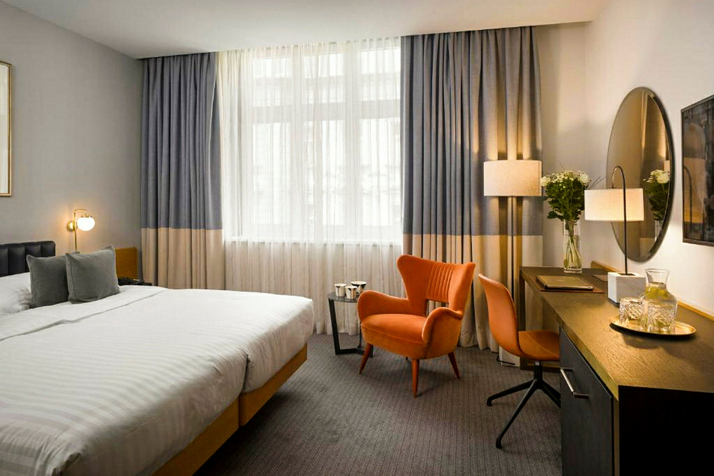 Et hotelværelse med en stor seng, en orange lænestol og skrivebord med spejl. (AI-genereret tekst)