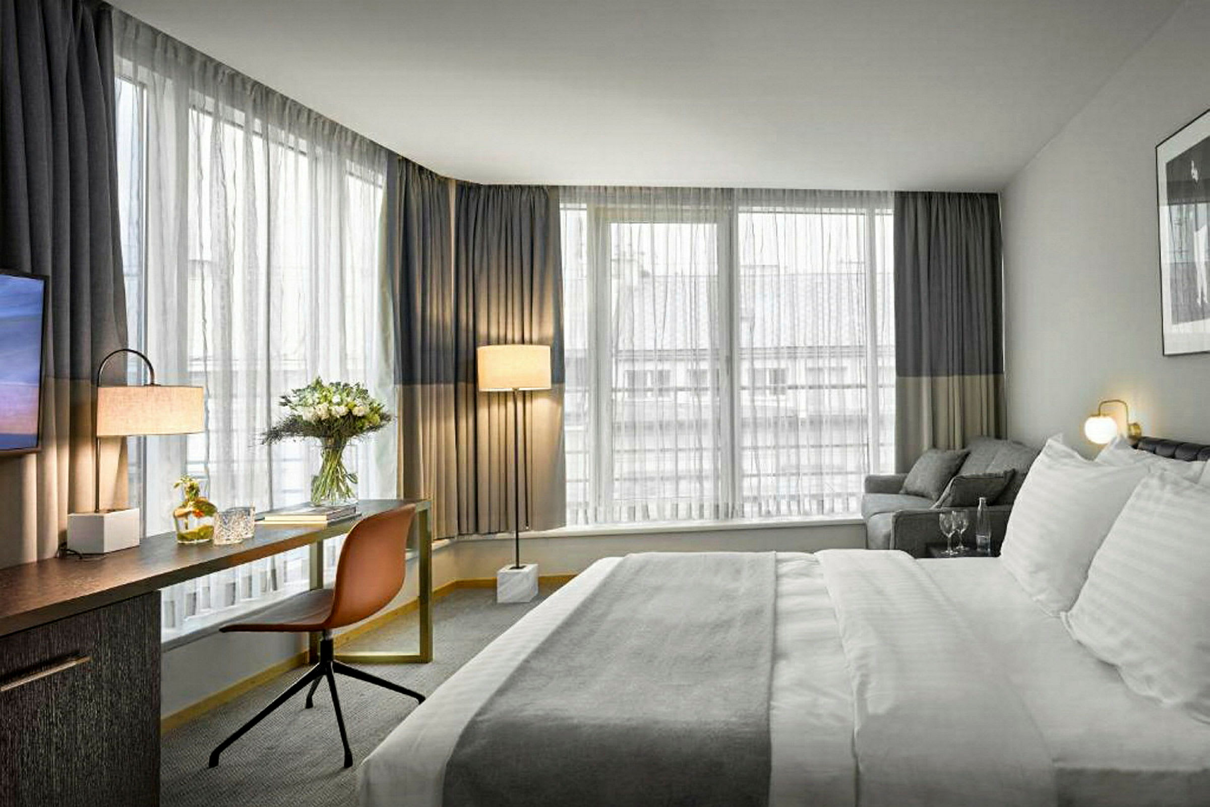 Et hotelværelse med stor seng, skrivebord, stol og vinduer med gardiner. (AI-genereret tekst)