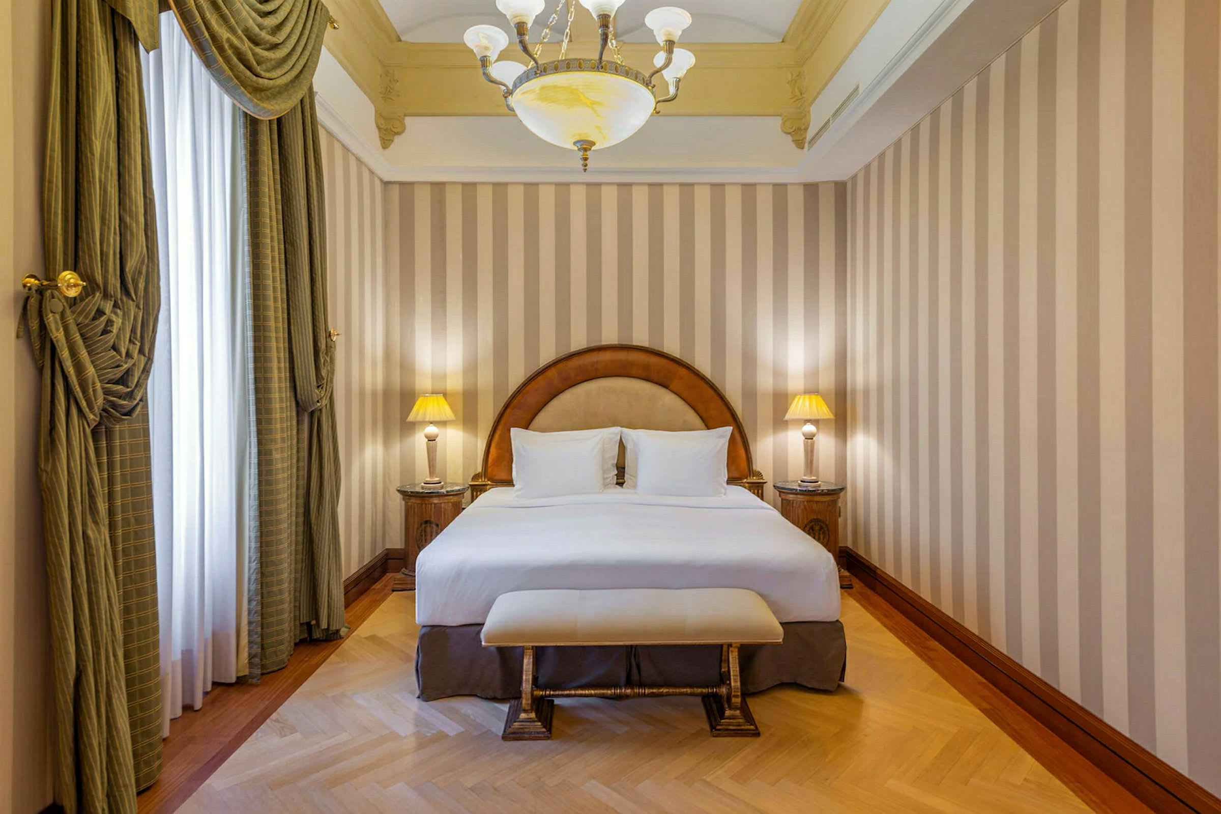 Et hotelværelse med en dobbeltseng, to natborde med lamper, og elegante gardiner foran vinduet. (AI-genereret tekst)