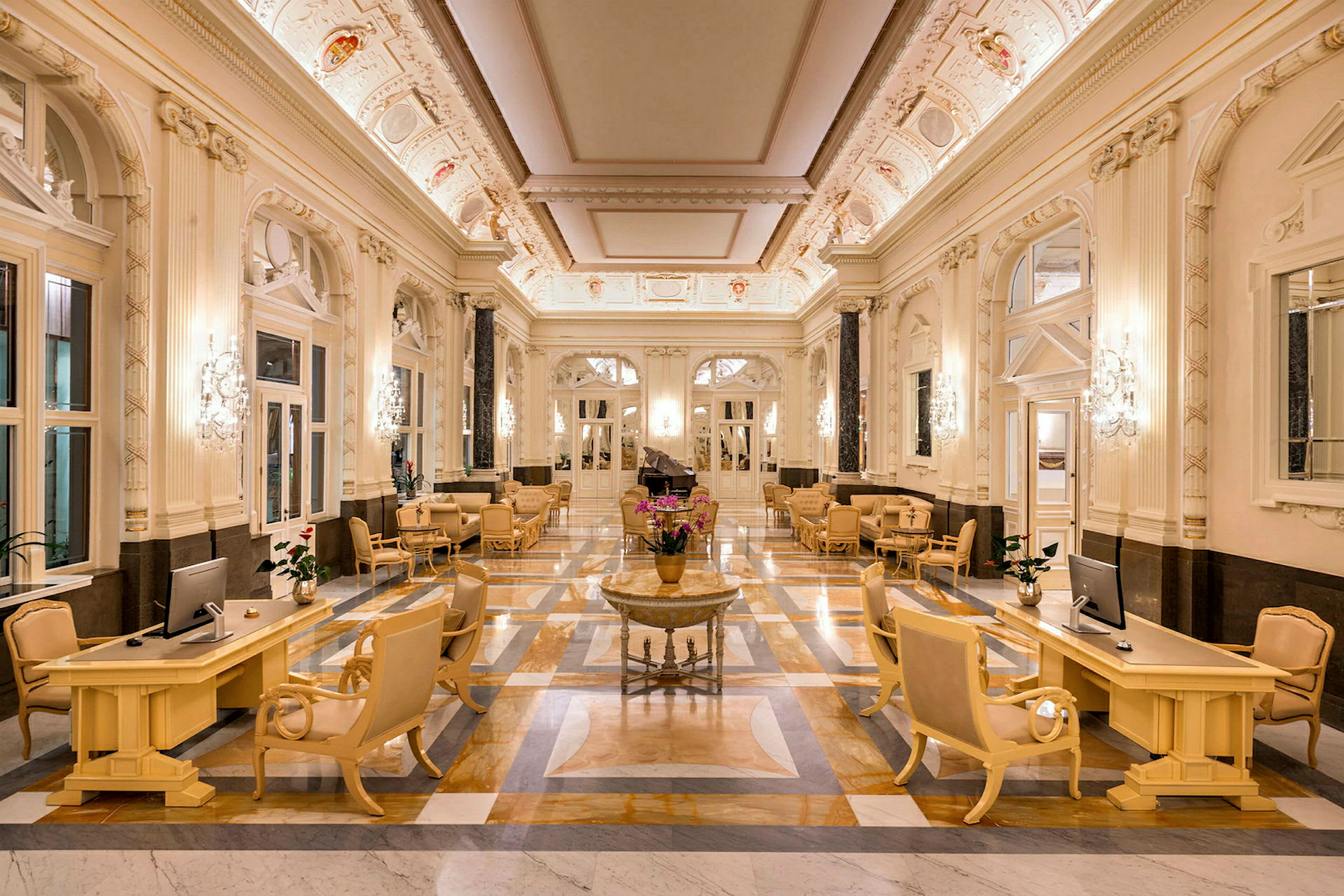 En elegant hotellobby med marmorgulv, stilfulde møbler og dekorativt udsmykket loftpanel. (AI-genereret tekst)