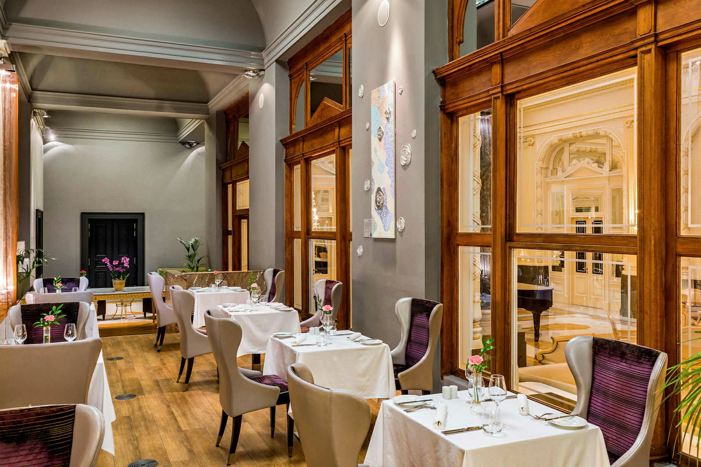 Billedet viser en elegant indrettet restaurant med moderne stole og borde dækket med hvide duge. Store vinduer og trædetaljer giver et luksuriøst indtryk. (AI-genereret tekst)