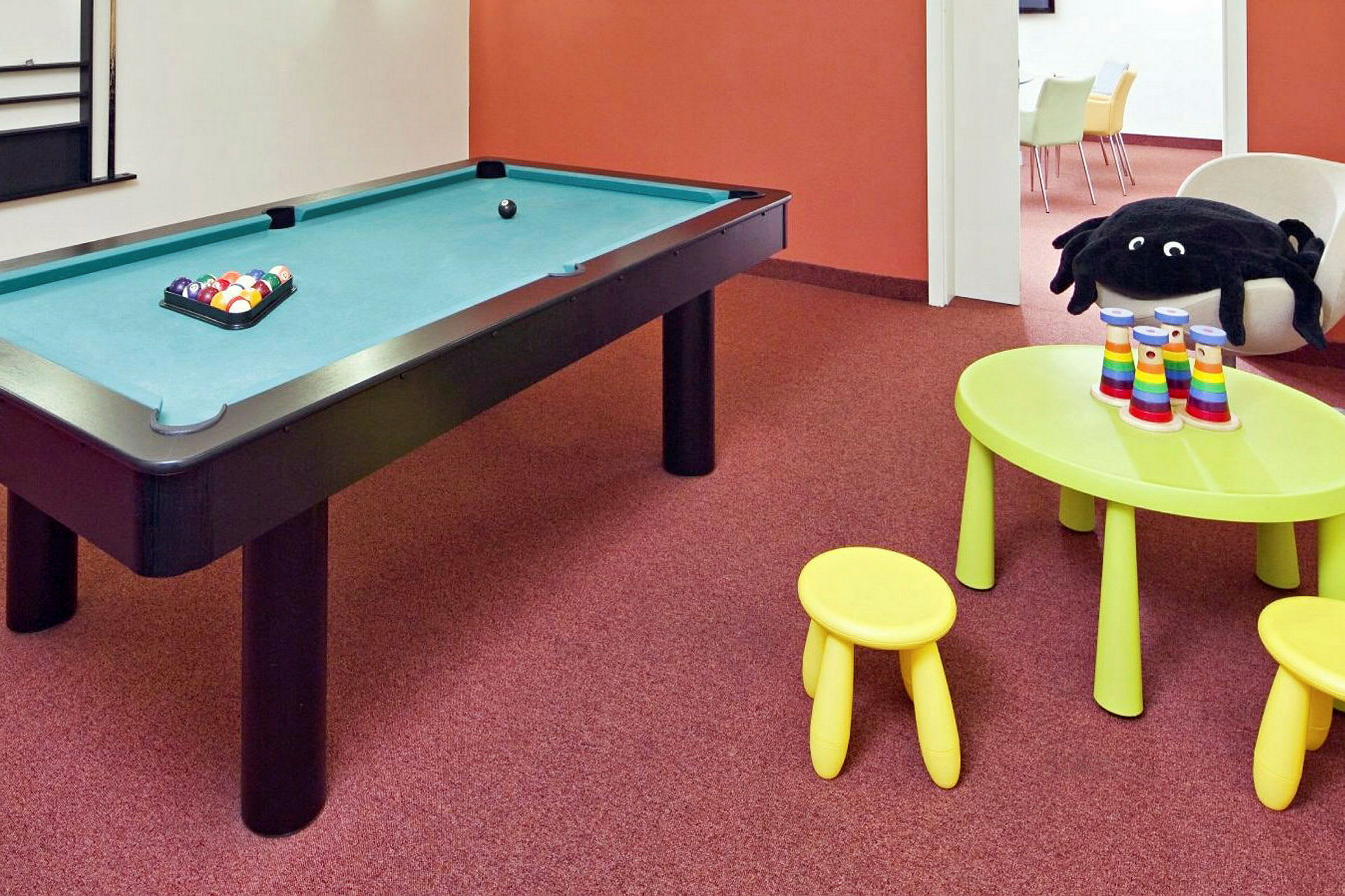Et rum med et billiardbord og et legeområde med gule møbler og farverige legetøj. (AI-genereret tekst)