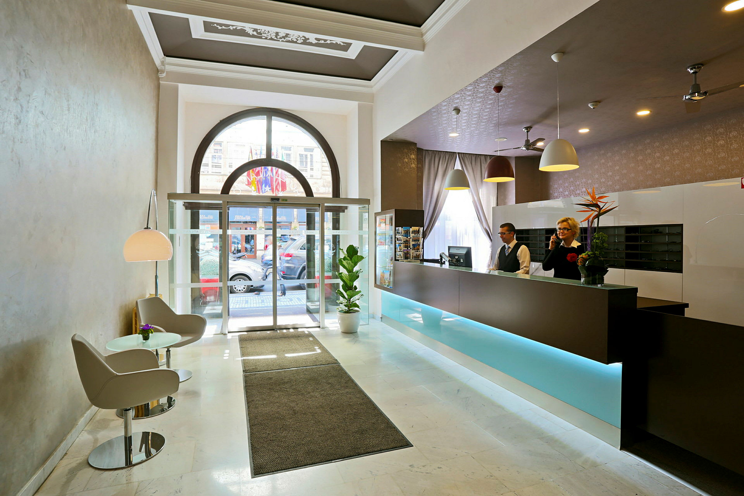 Hotellobby med reception, siddeområde og glasdøre mod ydersiden. (AI-genereret tekst)