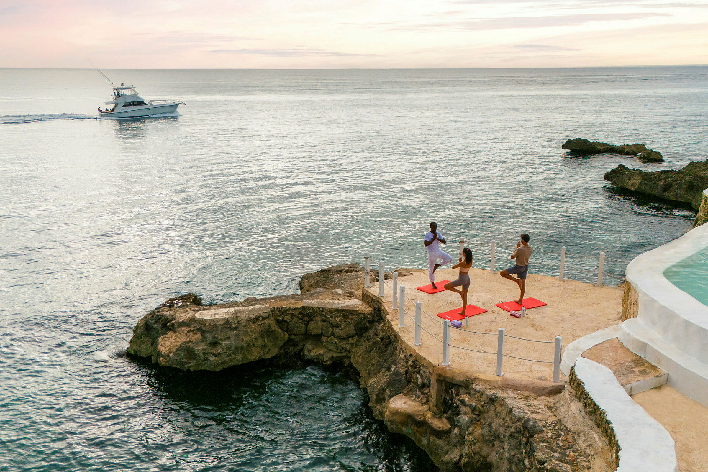 Personer, der dyrker yoga ved havet på en klippe, med en båd på vandet i baggrunden. (AI-genereret tekst)