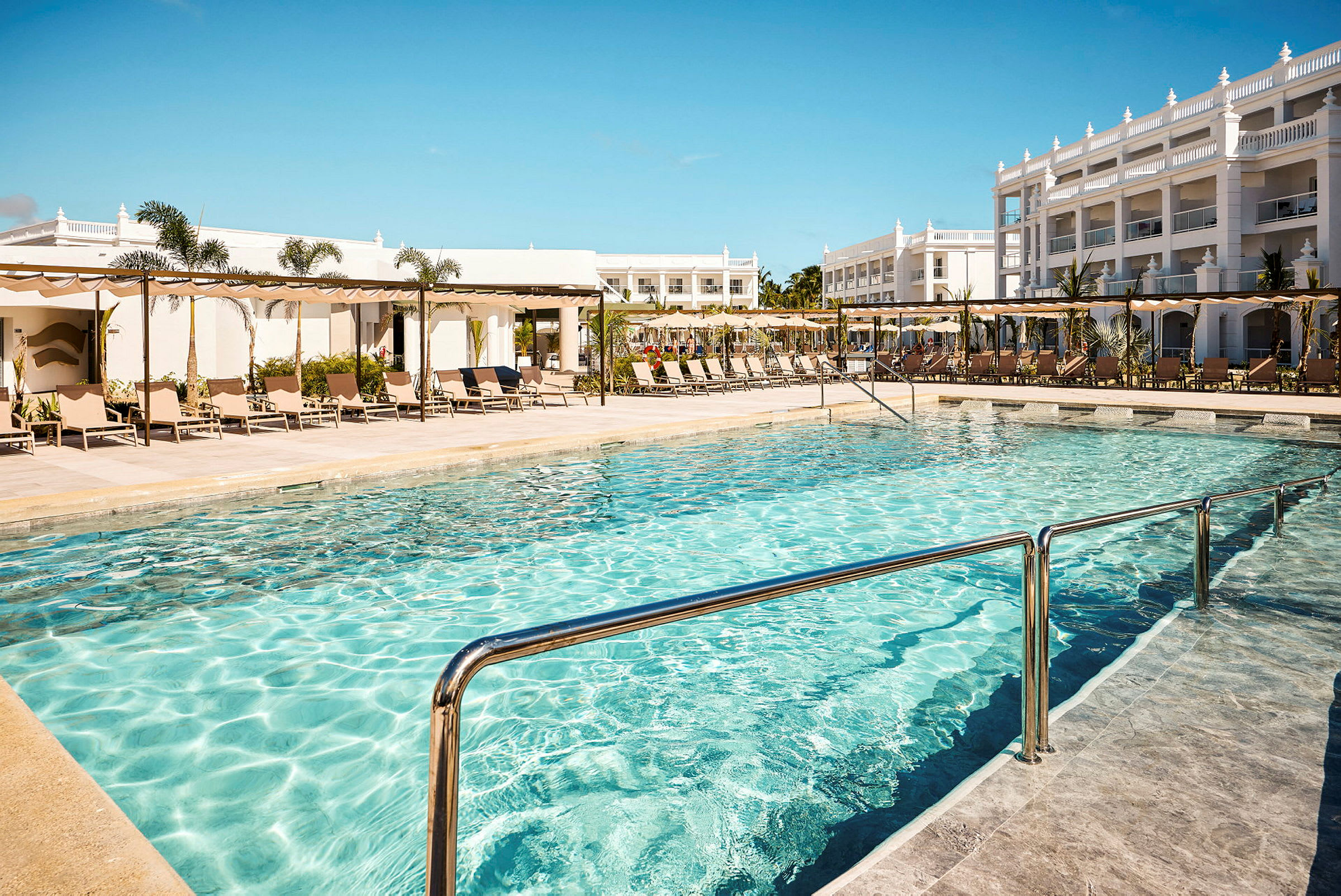 Udendørs pool med liggestole og hotelbygninger i baggrunden. (AI-genereret tekst)