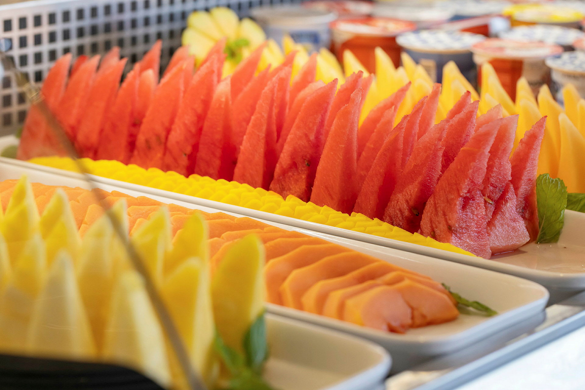 Skåret frugt som melon, papaya og ananas arrangeret på fade. (AI-genereret tekst)