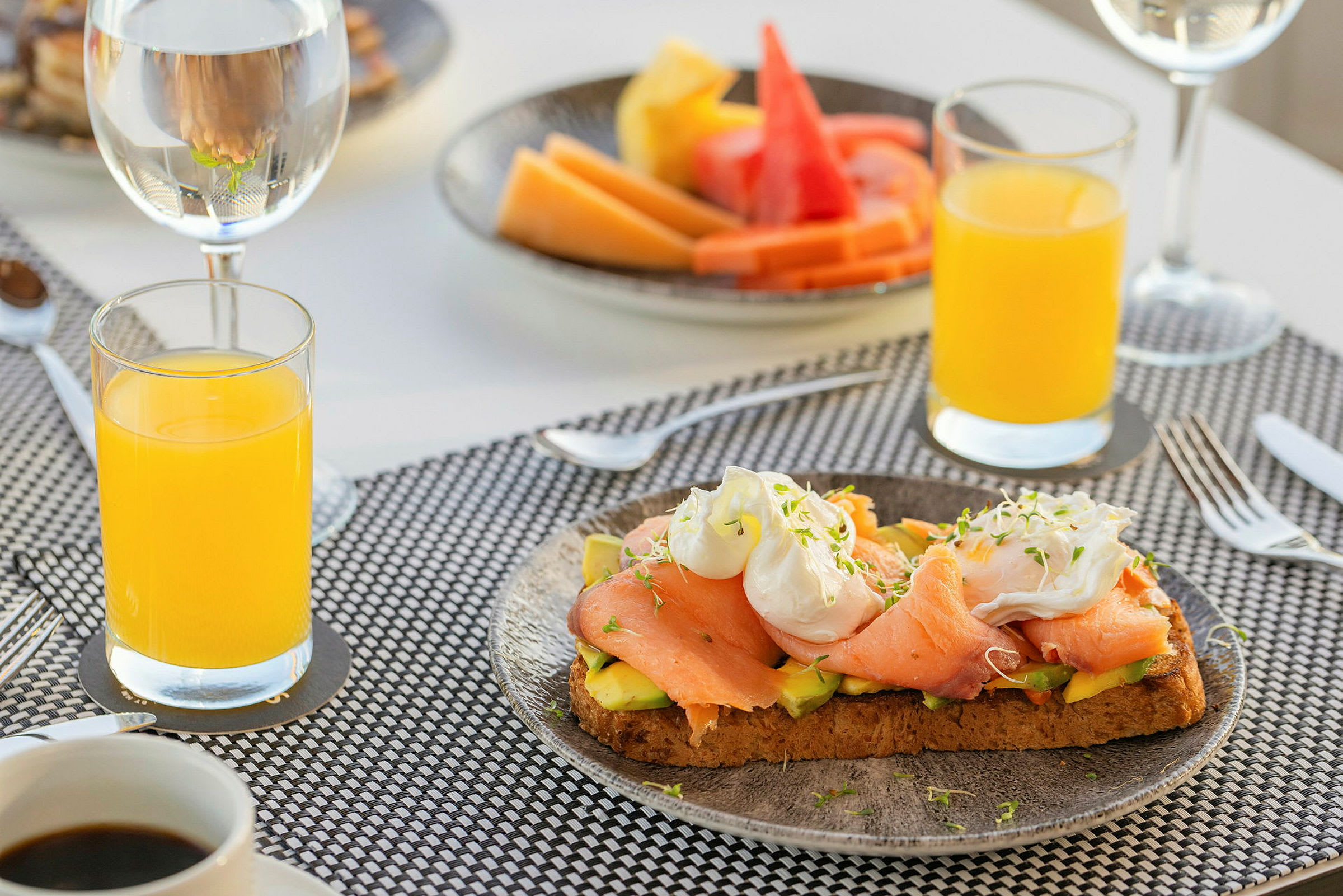En morgenmad med juice, kaffe, toast med laks og avocado og en tallerken med frugt. (AI-genereret tekst)