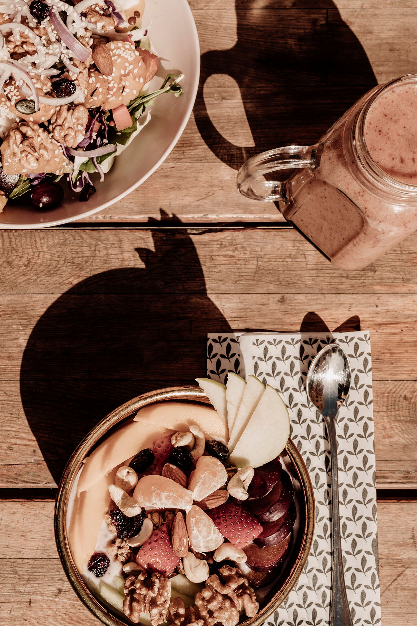 Et måltid med blandet salat og en skål fyldt med frugt og nødder på et træbord. (AI-genereret tekst)