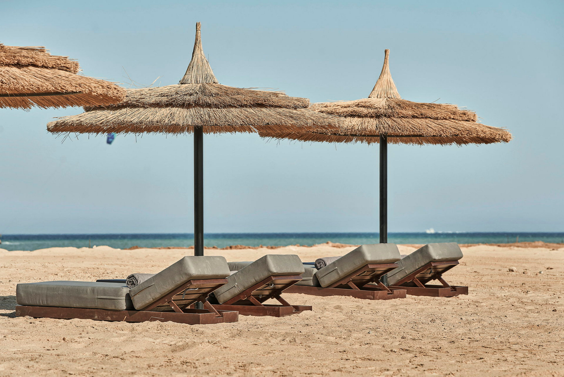 Liggestole med stråtag på sandstrand med hav i baggrunden. (AI-genereret tekst)