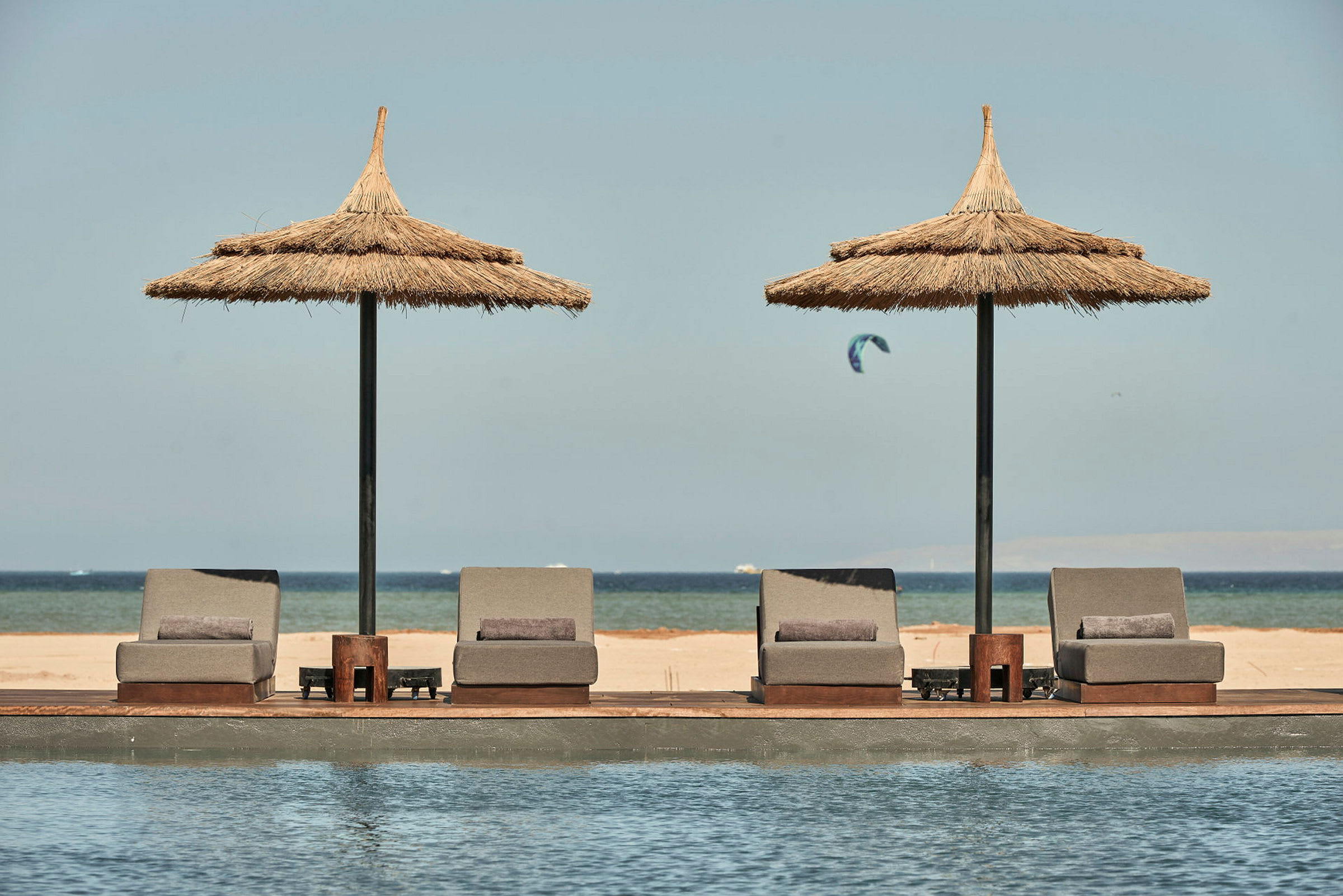 Liggestole og parasoller ved en pool med udsigt til stranden og havet. (AI-genereret tekst)