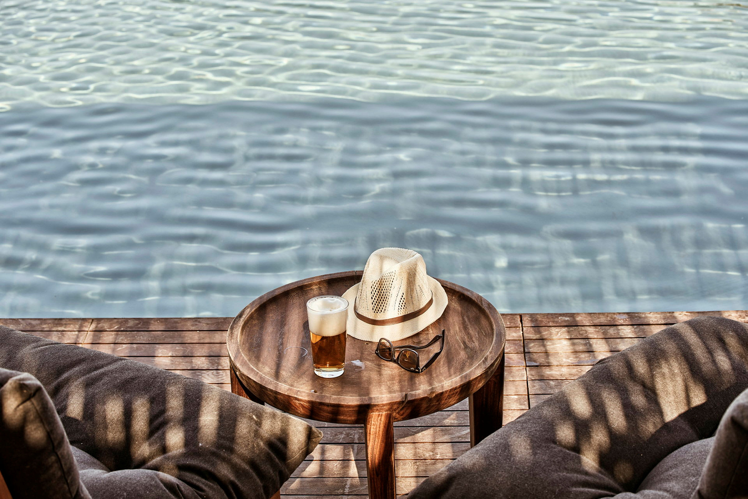 Et bord ved en pool med en hat, solbriller og et glas drik. (AI-genereret tekst)