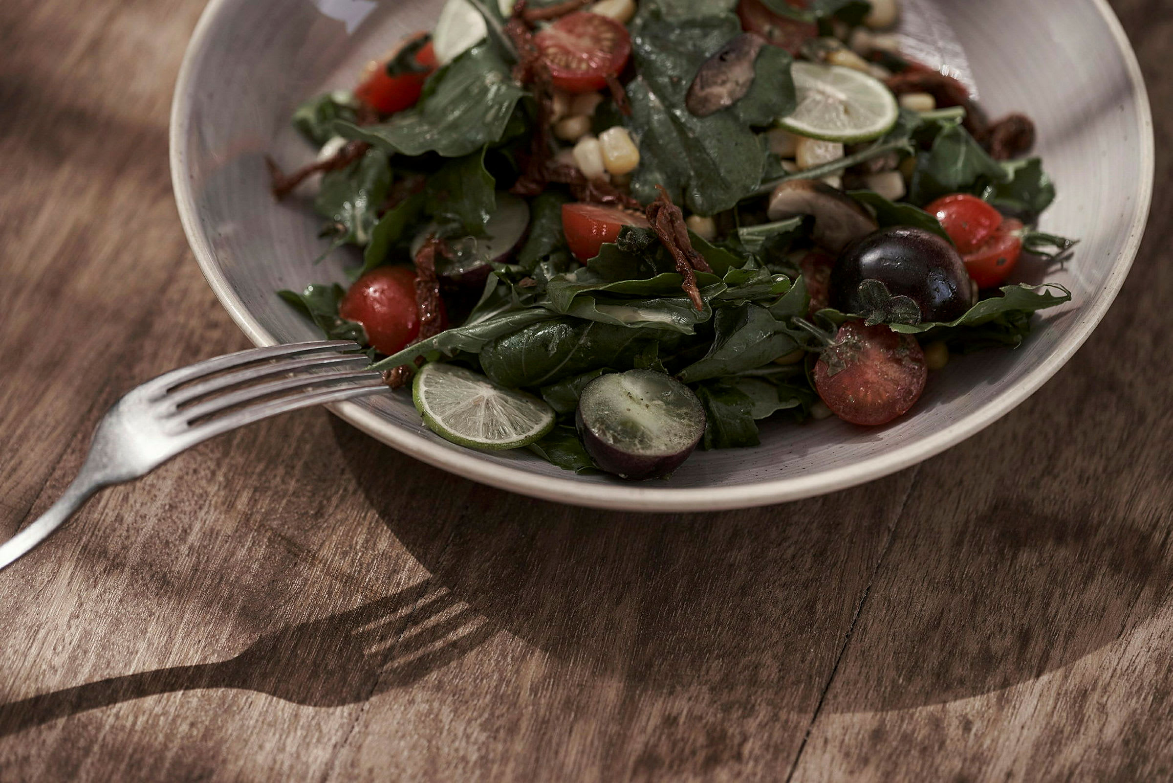 En salat med forskellige grøntsager og frugter serveret på en tallerken med en gaffel ved siden af. (AI-genereret tekst)